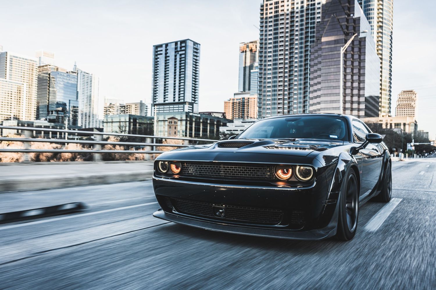 Black Dodge Challenger Hellcat in motion against urban skyline backdrop.