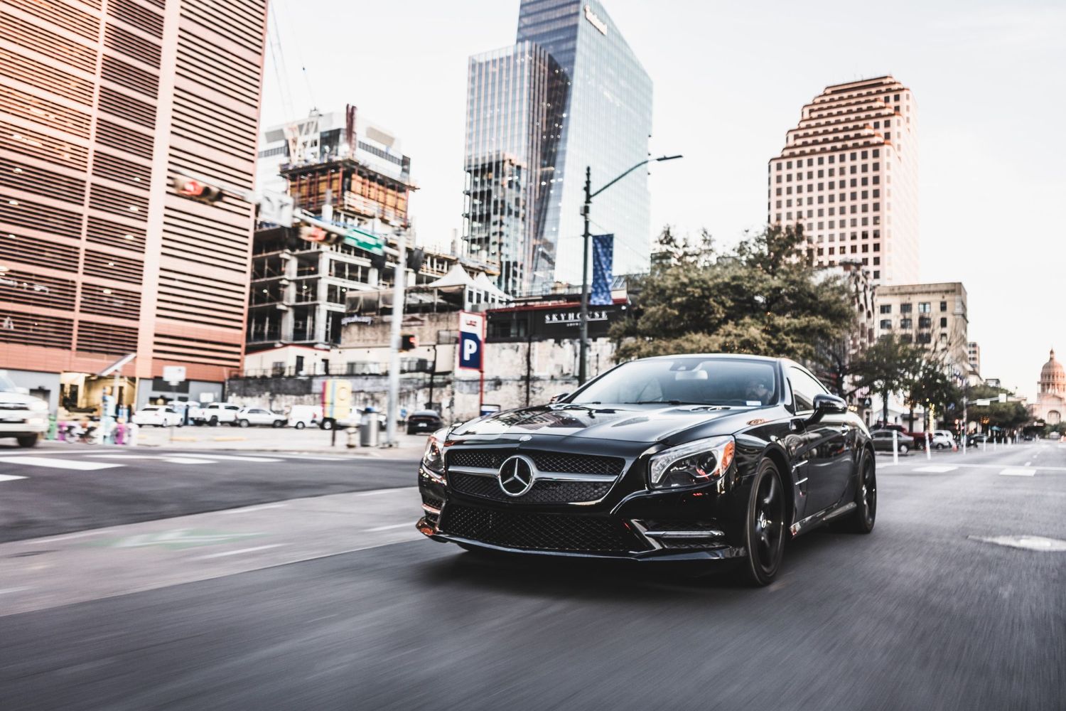 Black Mercedes sports car driving through downtown intersection with skyscrapers.