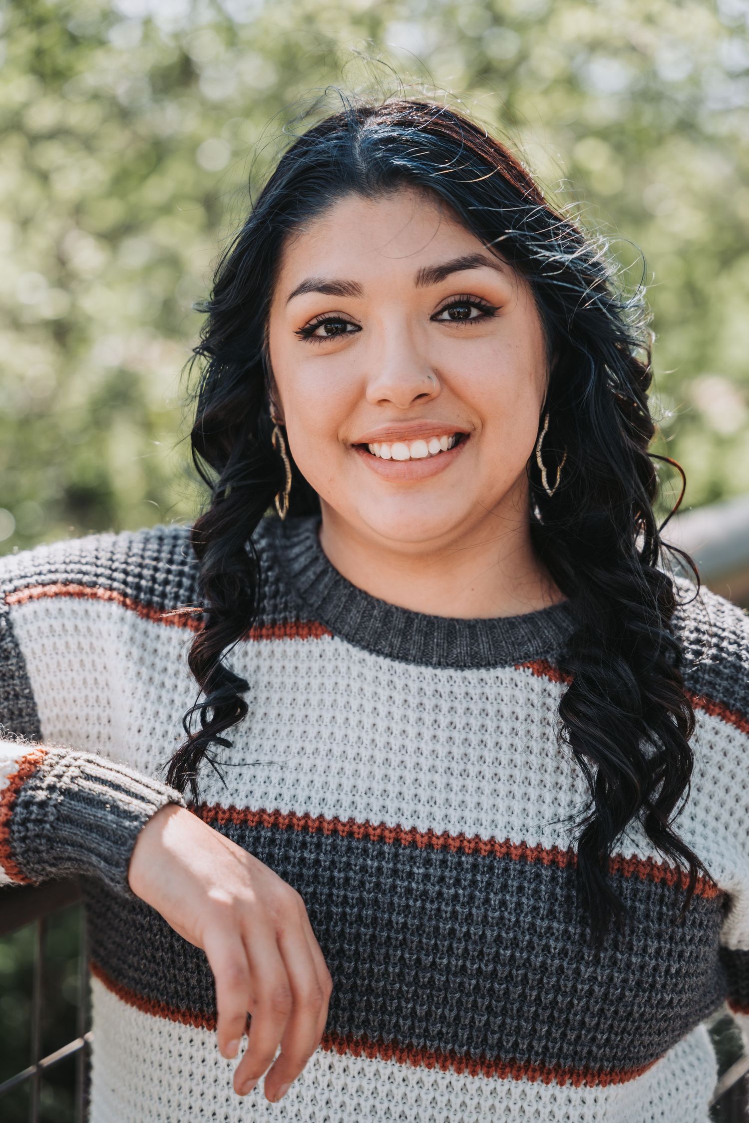 Portrait outdoors with someone wearing a striped sweater and long dark wavy hair in natural lighting.