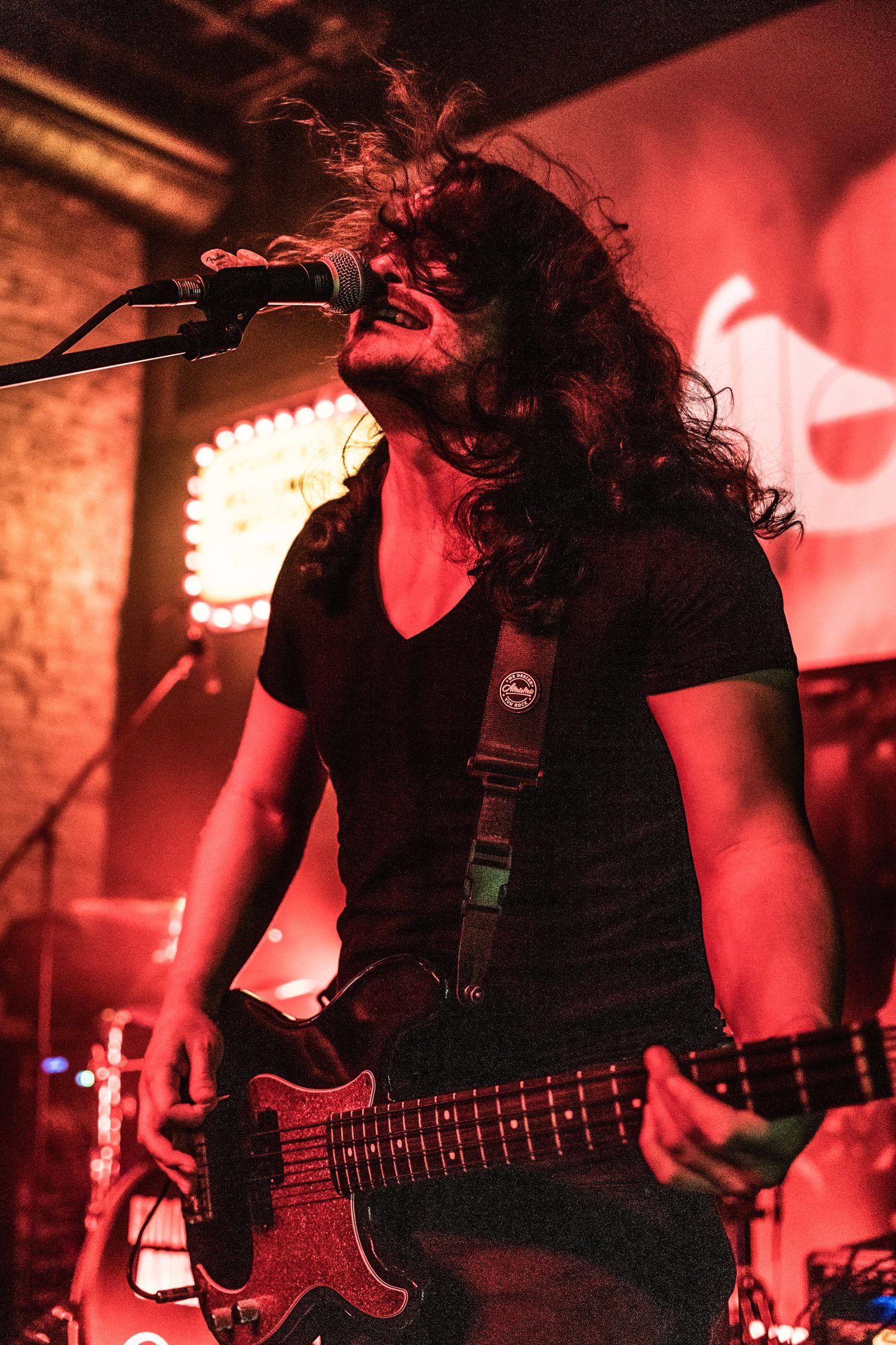 Energetic bassist with long dark hair performs under red stage lighting.