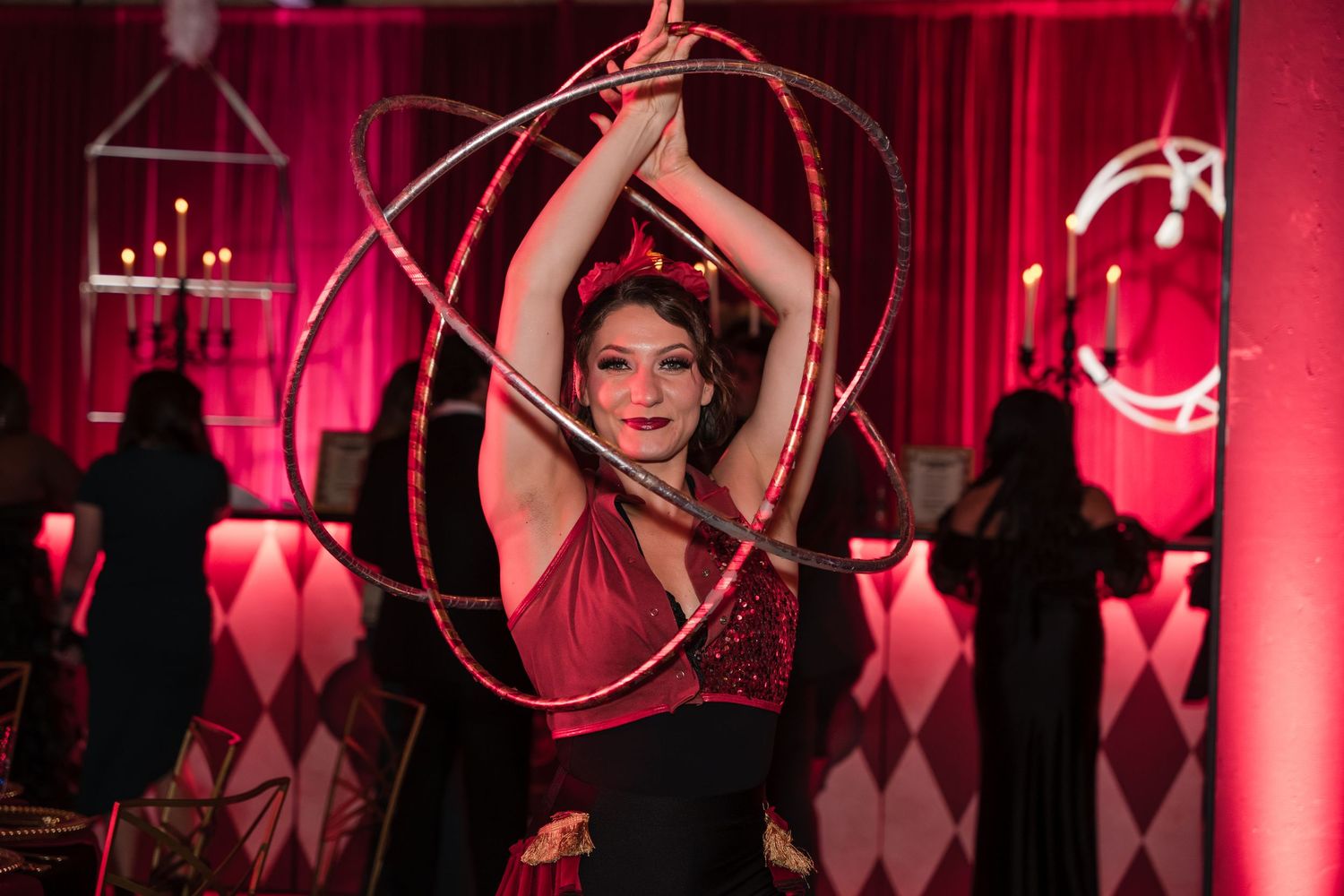 Performers in black costumes dance on stage with dramatic red lighting and circular props in a theatrical show.