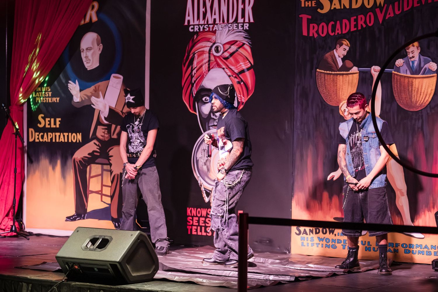 Musicians perform on stage at a live entertainment venue with dramatic red lighting and theatrical atmosphere.