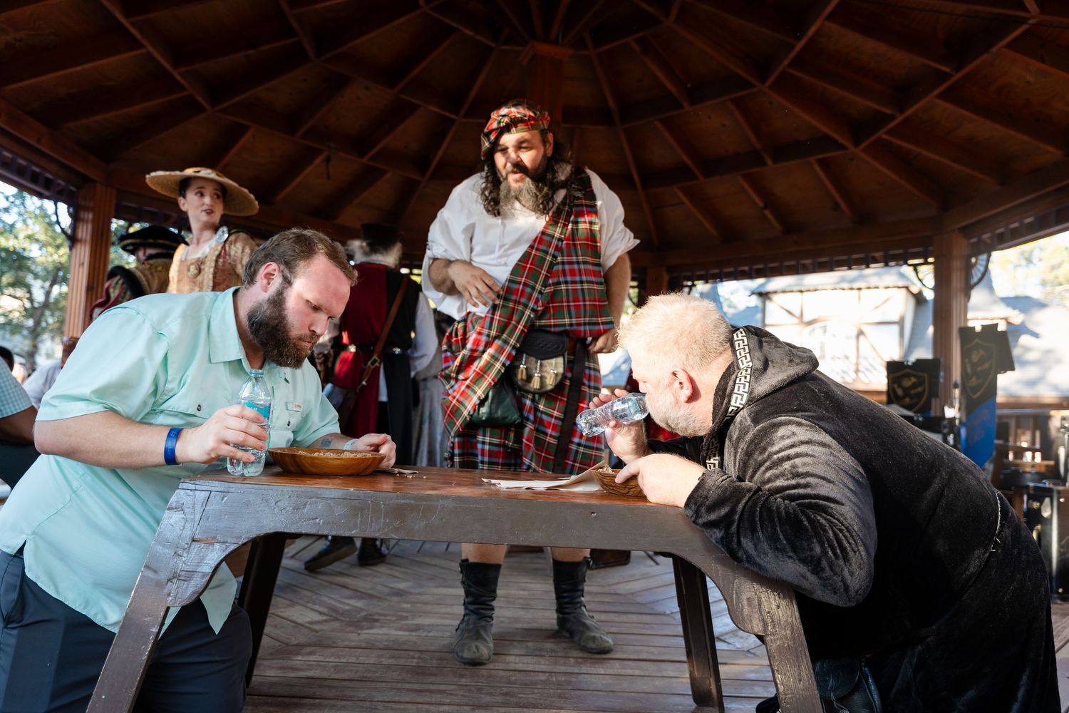 People enjoying drinks and socializing at a rustic outdoor pavilion bar during a gathering.