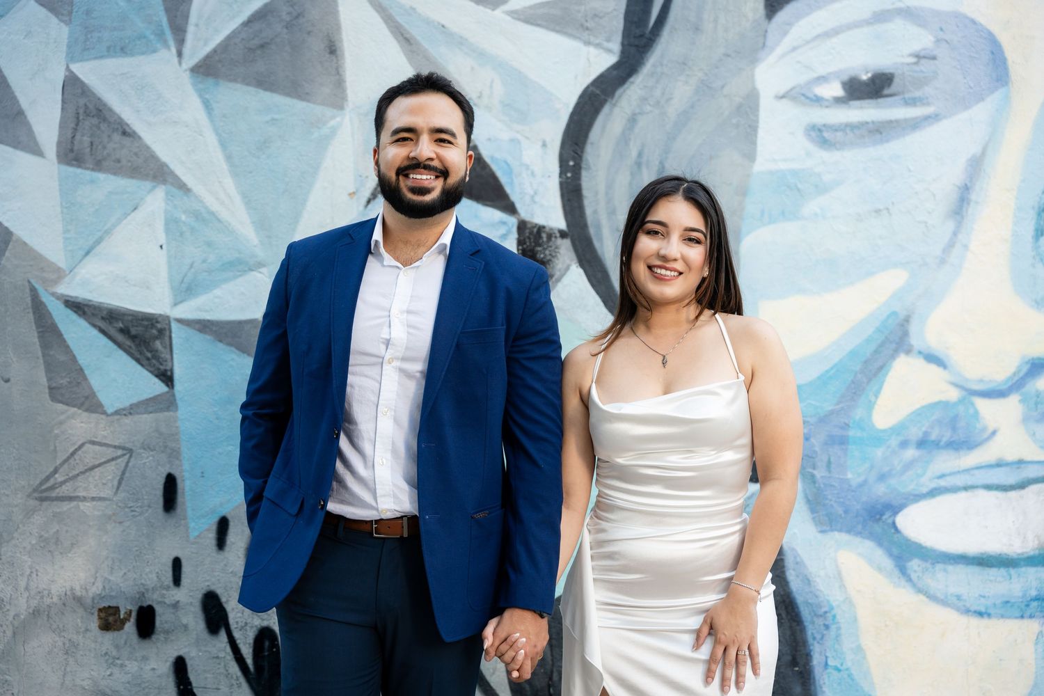 Couple poses against geometric blue wall backdrop in formal attire for stylish engagement photos.