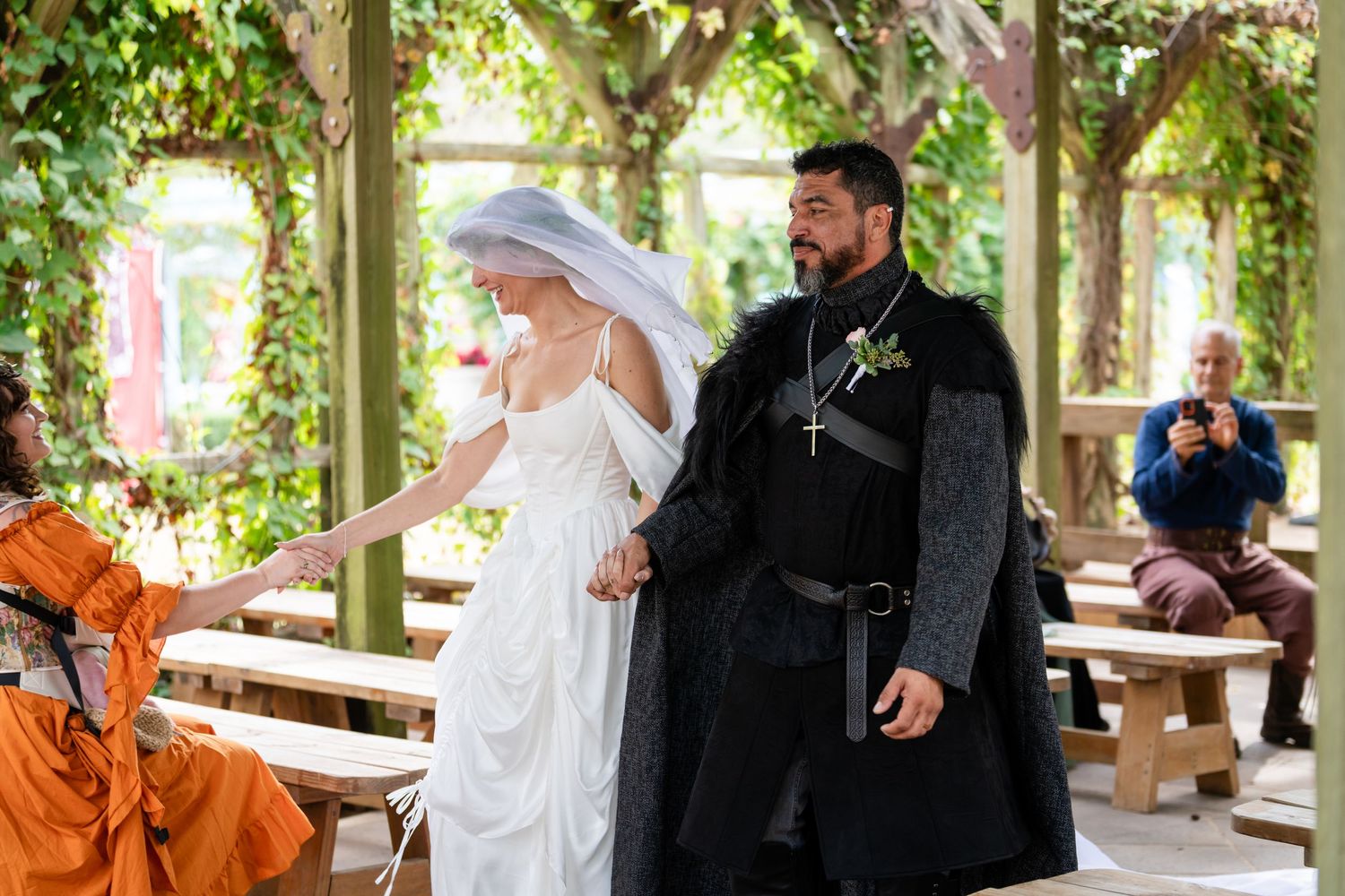 A couple shares a romantic moment under a vine-covered pergola in an outdoor garden setting.
