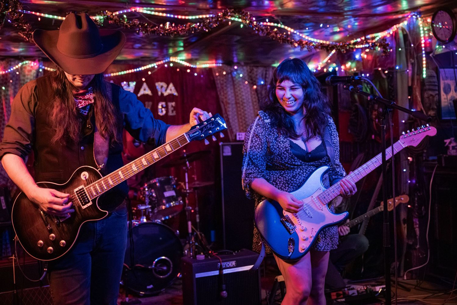 Musicians perform on stage at a nightclub with colorful purple and red lighting illuminating the performance area.