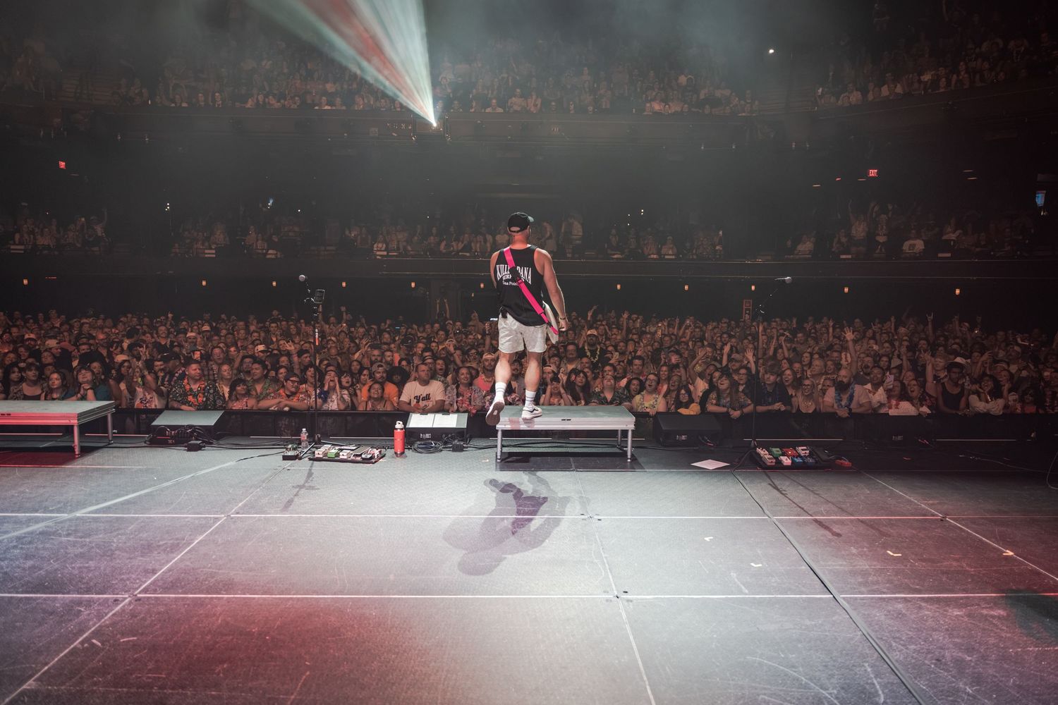 Performer stands on stage before massive arena crowd with dramatic lighting at a packed concert venue.