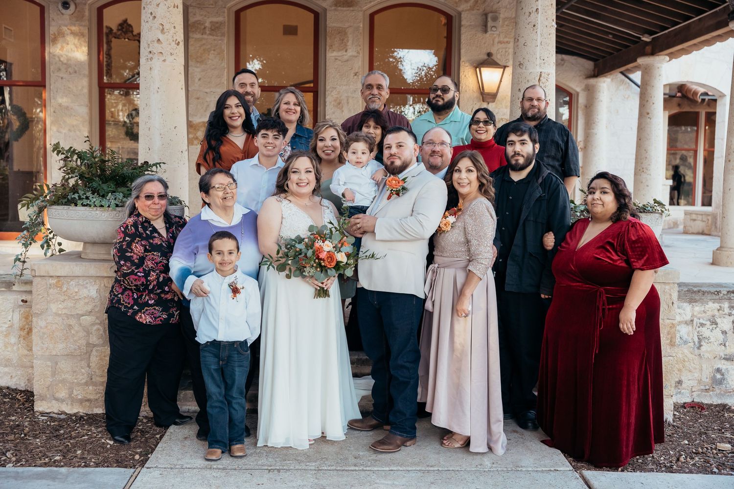 Large wedding party poses together on stone porch with architectural columns.