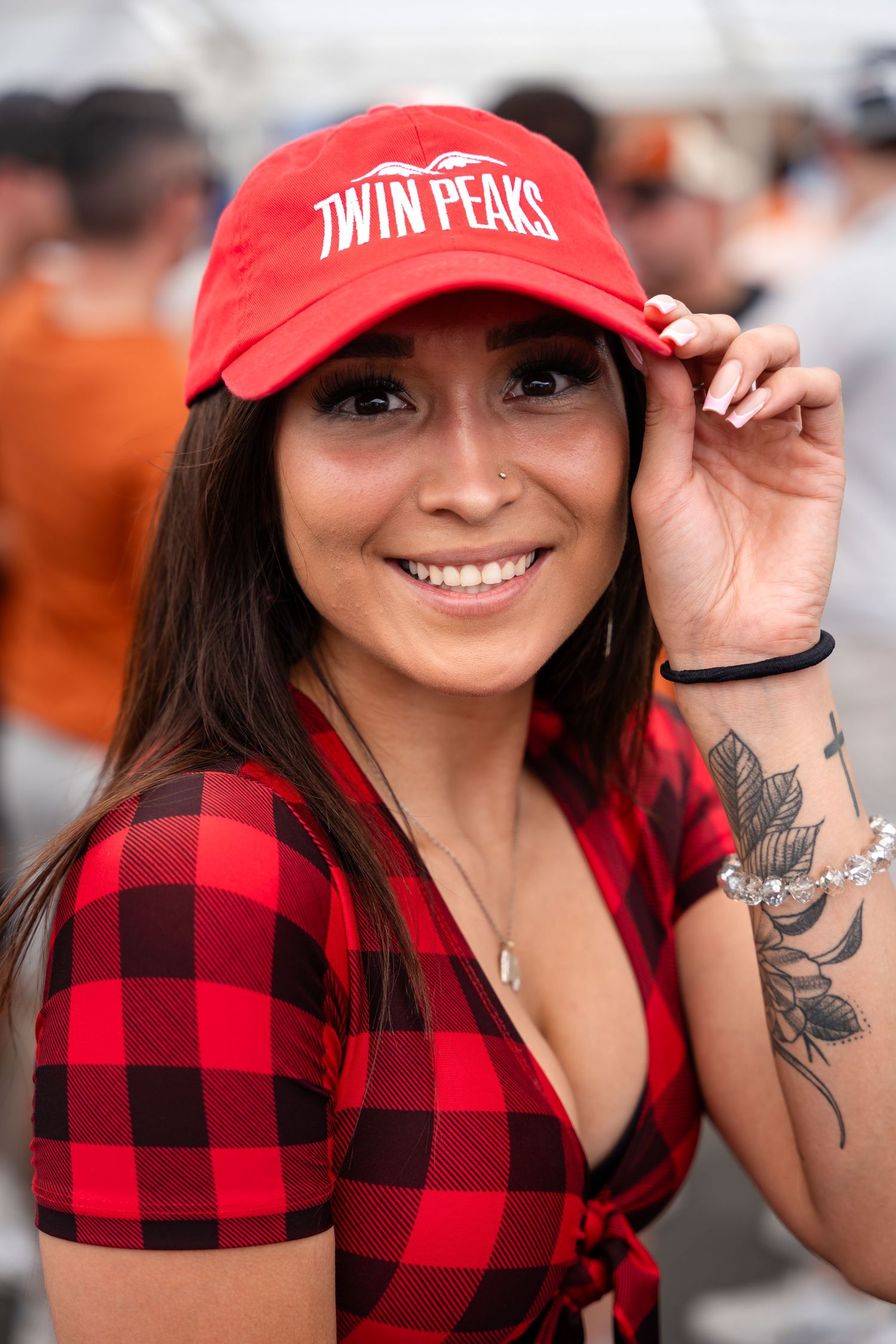 Person wearing red buffalo plaid shirt and Twin Peaks baseball cap smiles at outdoor event.