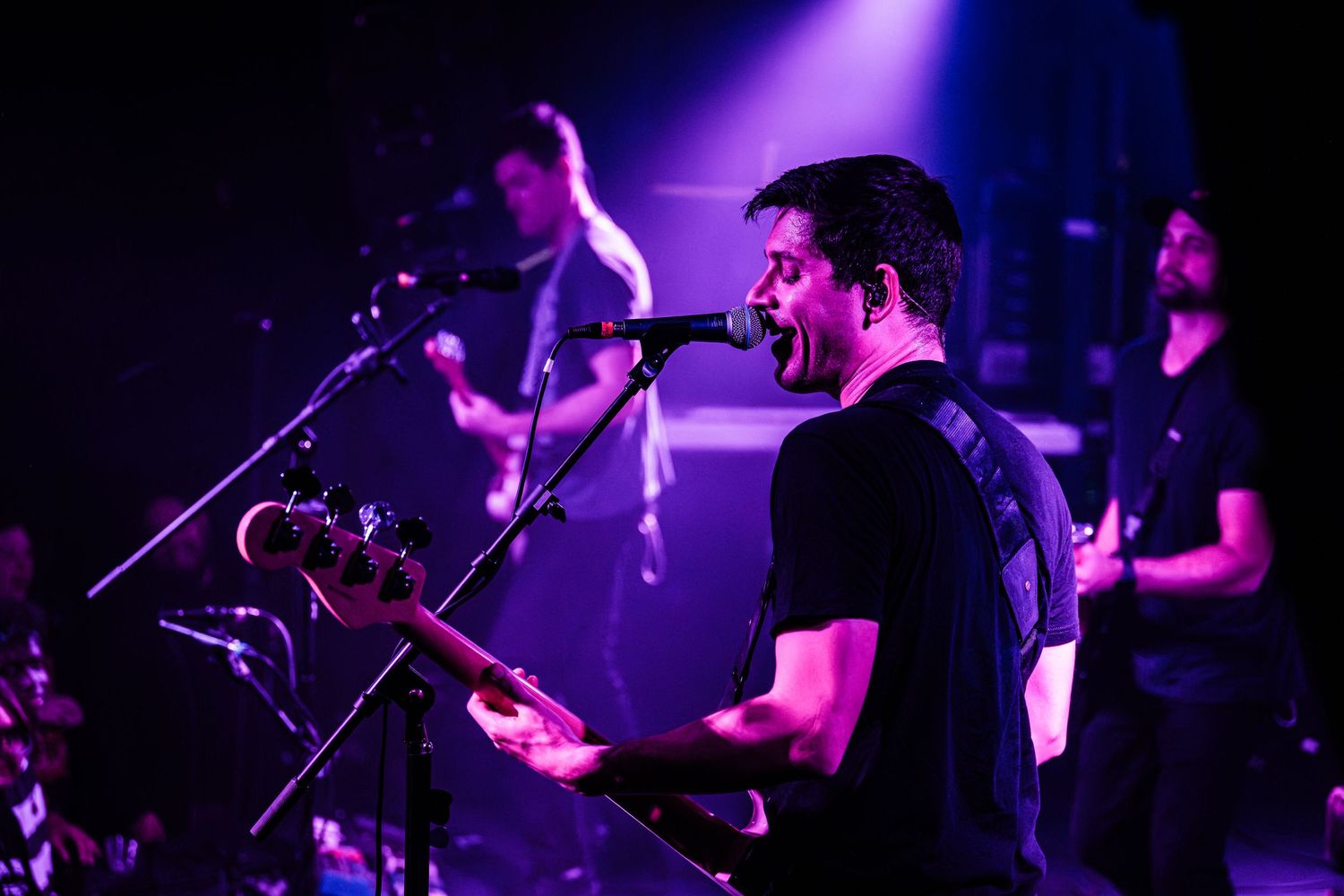 Musicians perform on a dark stage with dramatic purple lighting during a live concert performance.
