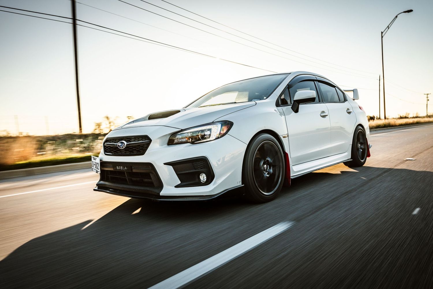 Modified white Subaru sedan with custom wheels photographed during rolling shot at dusk.