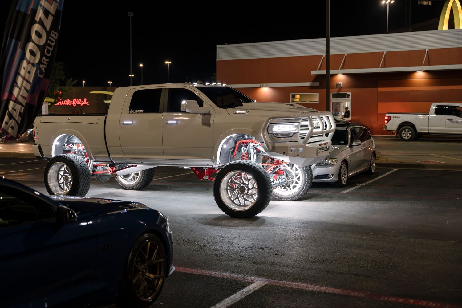 Custom truck with illuminated wheels displayed at night in a parking lot.