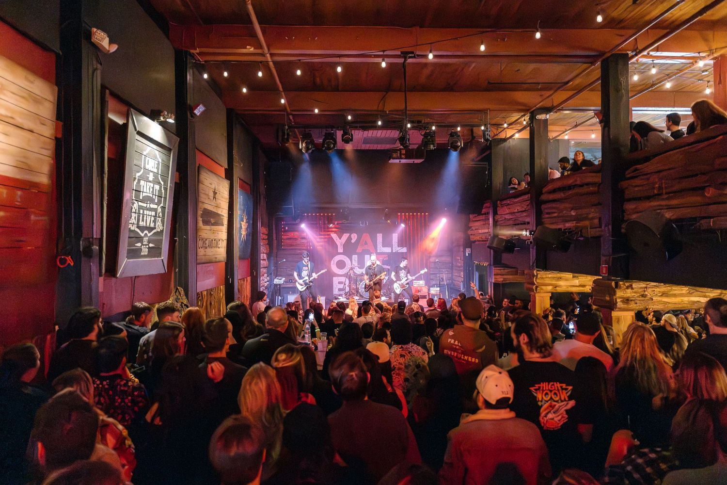 Packed concert venue with crowd watching performers on stage under warm lighting.