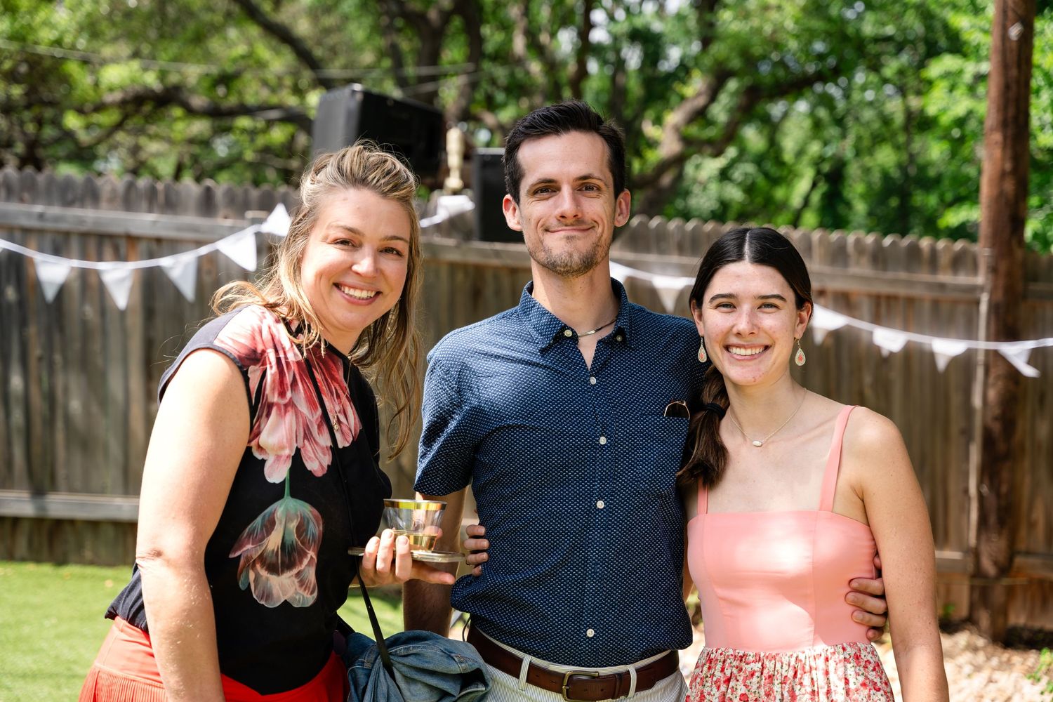 Three guests at outdoor party holding drinks and smiling together.
