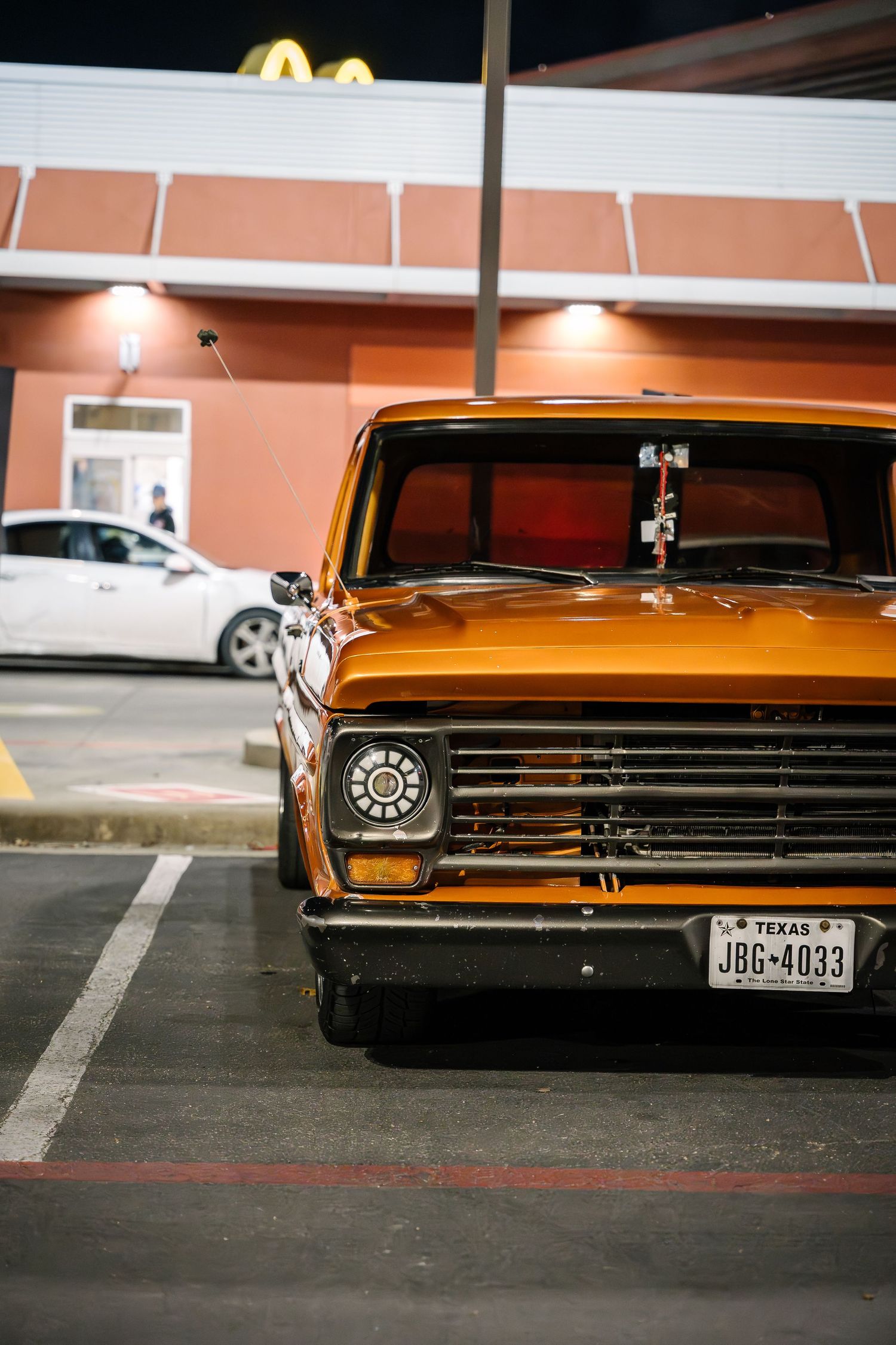 Classic orange Ford pickup truck parked outside McDonald's at night showing vintage styling.