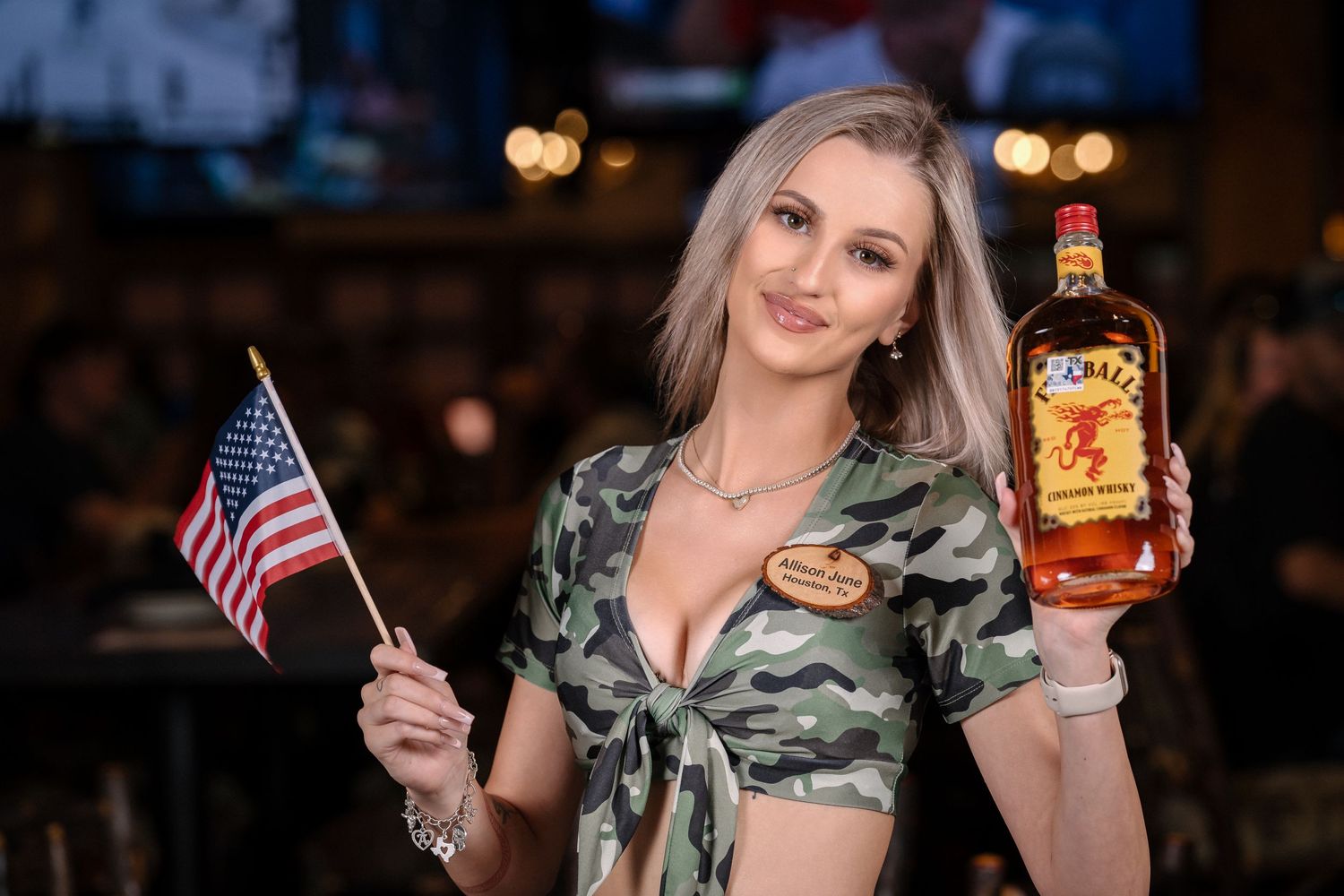Bar server holding American flag and whiskey bottle while wearing patriotic attire.