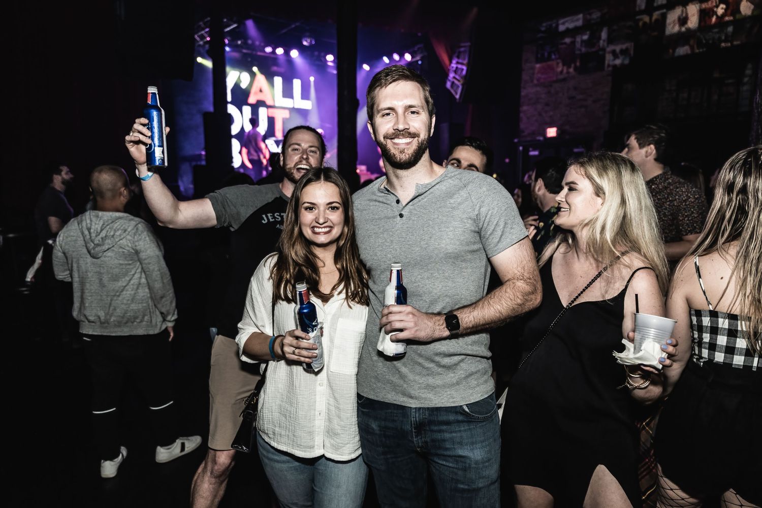 Concert attendees socializing and enjoying drinks at nightclub event with stage lighting.