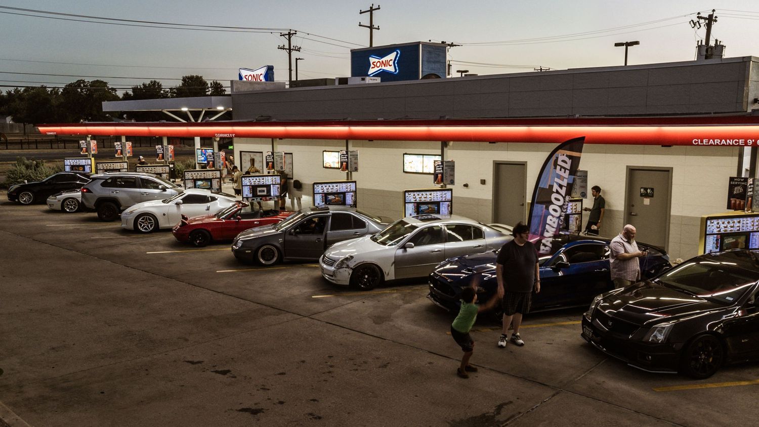 Cars parked in front of a retail building during a car meet at sunset.