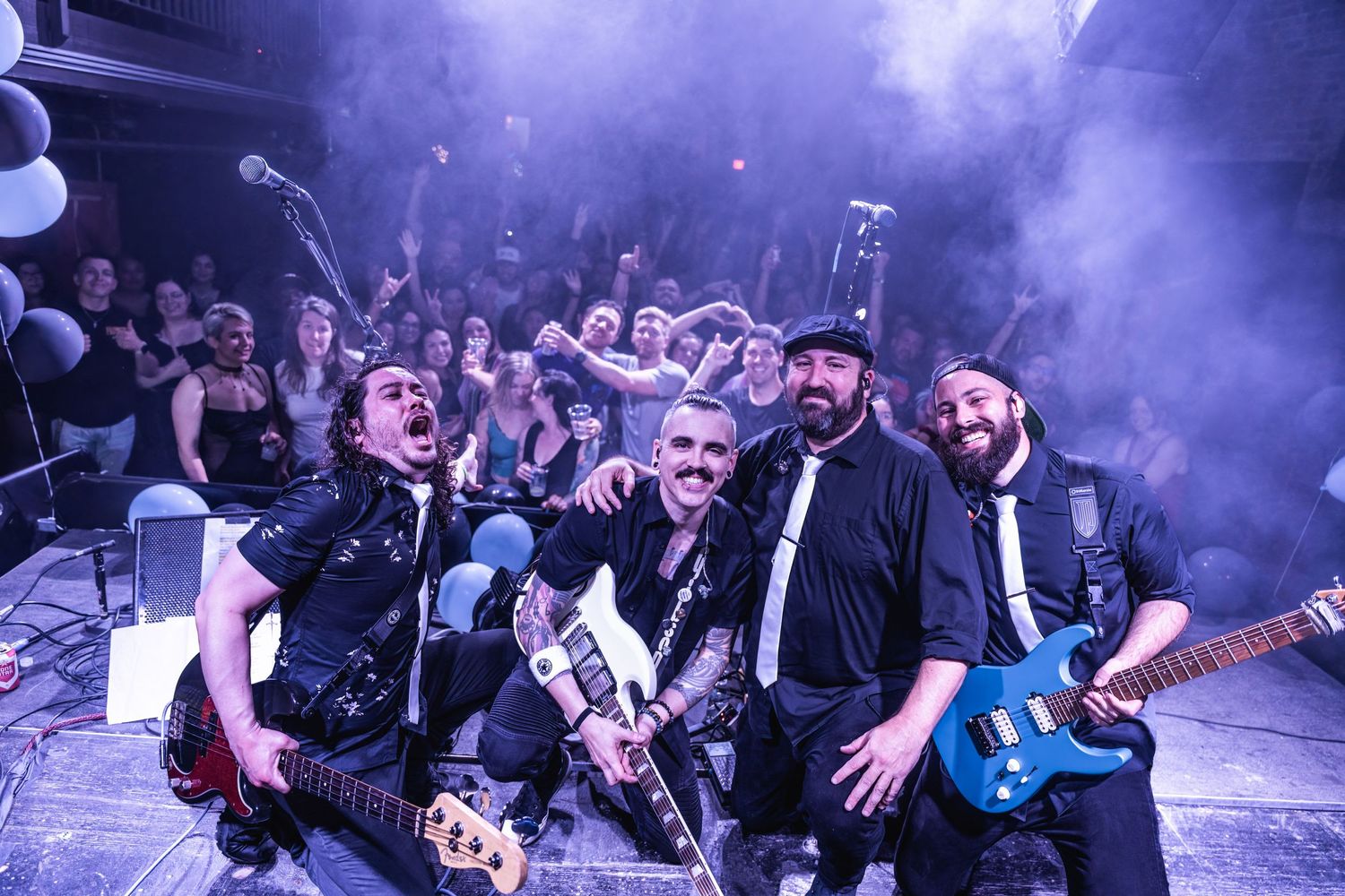 Band poses together on stage during concert performance with purple atmospheric lighting.