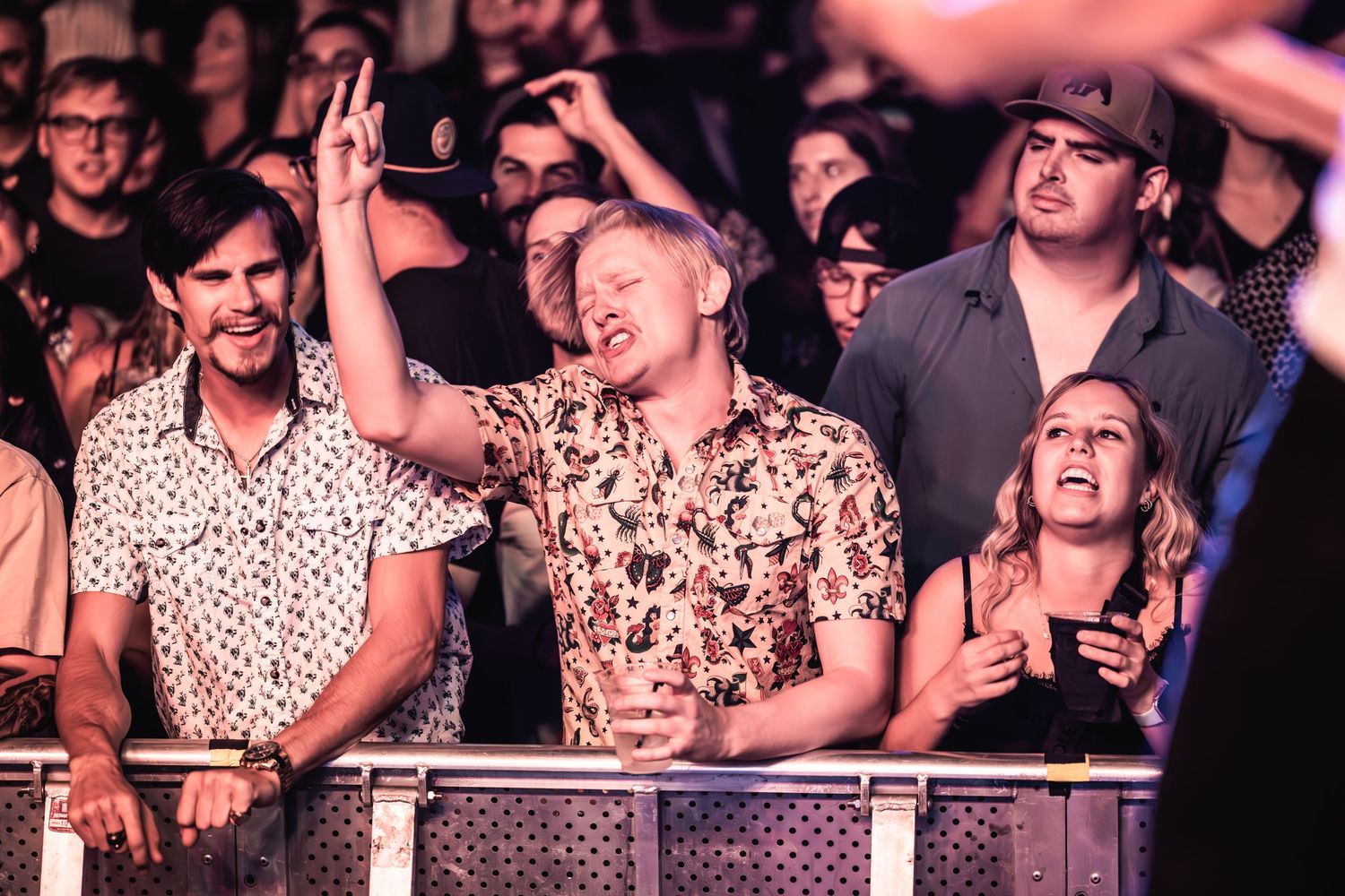 Music fans express joy while watching performance from behind venue barrier.