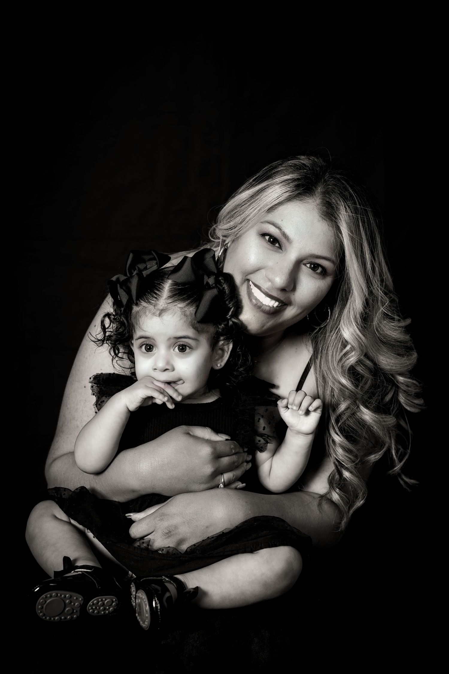 Intimate black and white portrait of a parent embracing young child in dark setting.