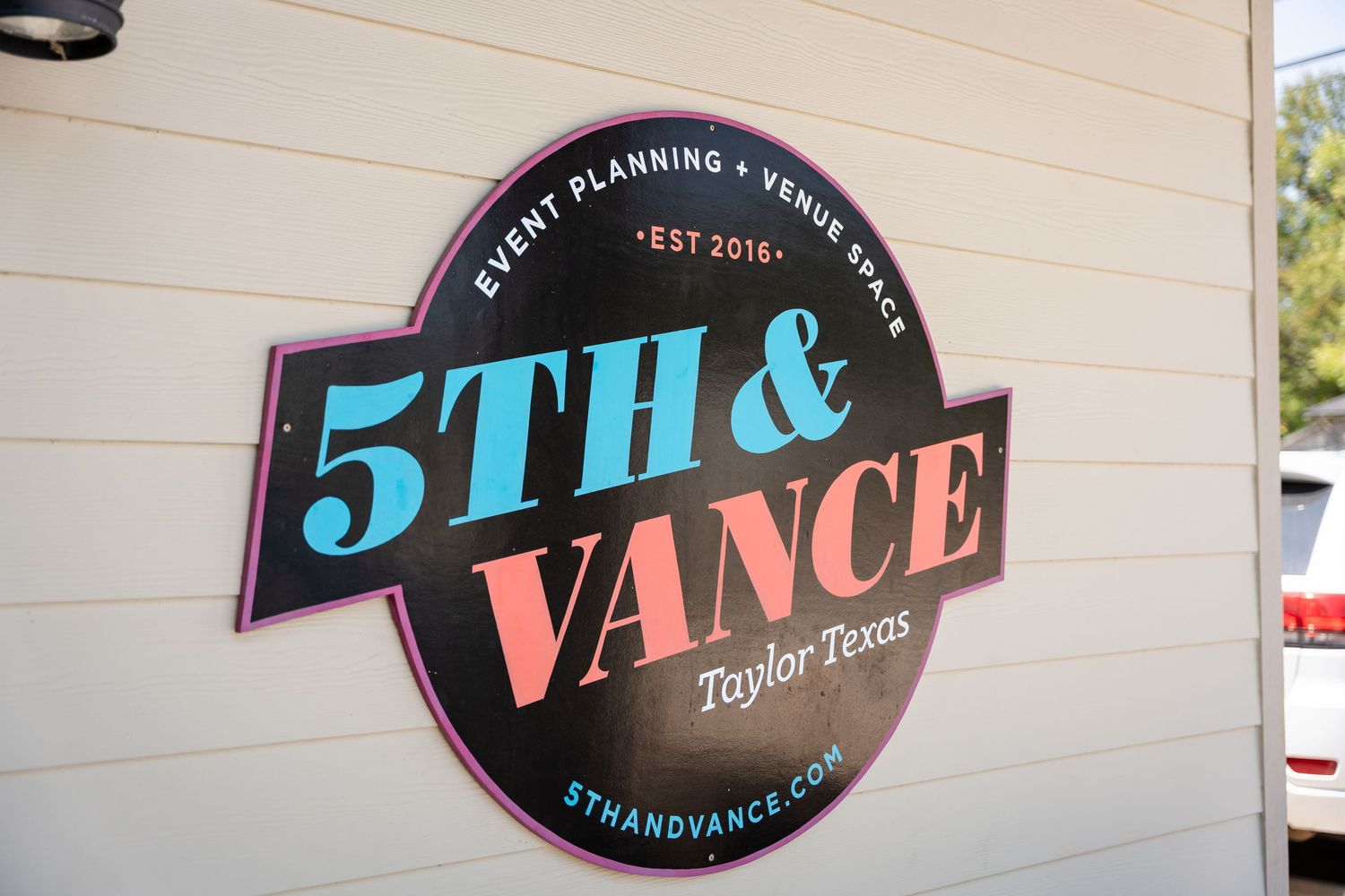 Black and coral colored business sign reading '5TH & VANCE' mounted on beige wall.