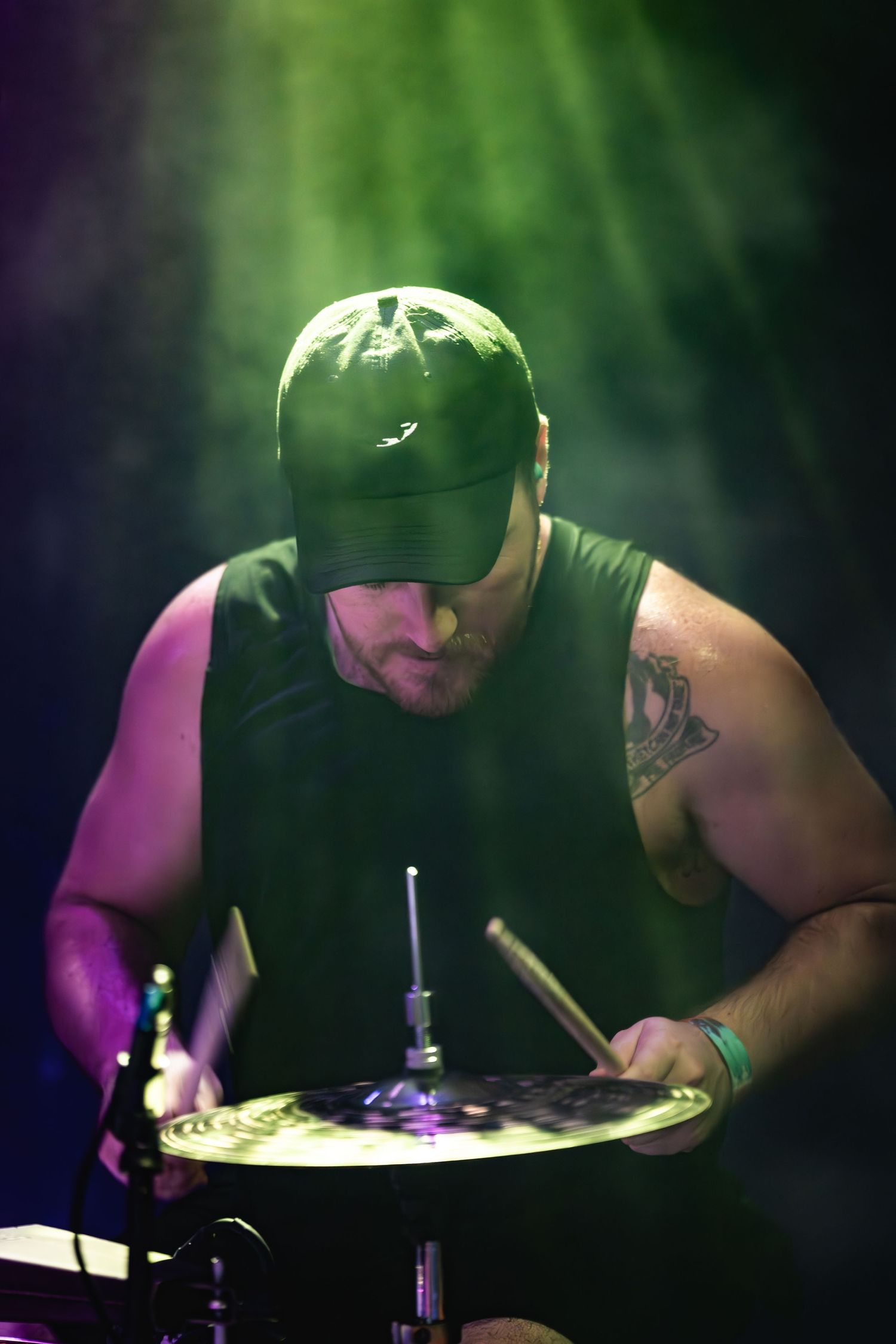 Drummer in baseball cap performs under dramatic green stage lighting.