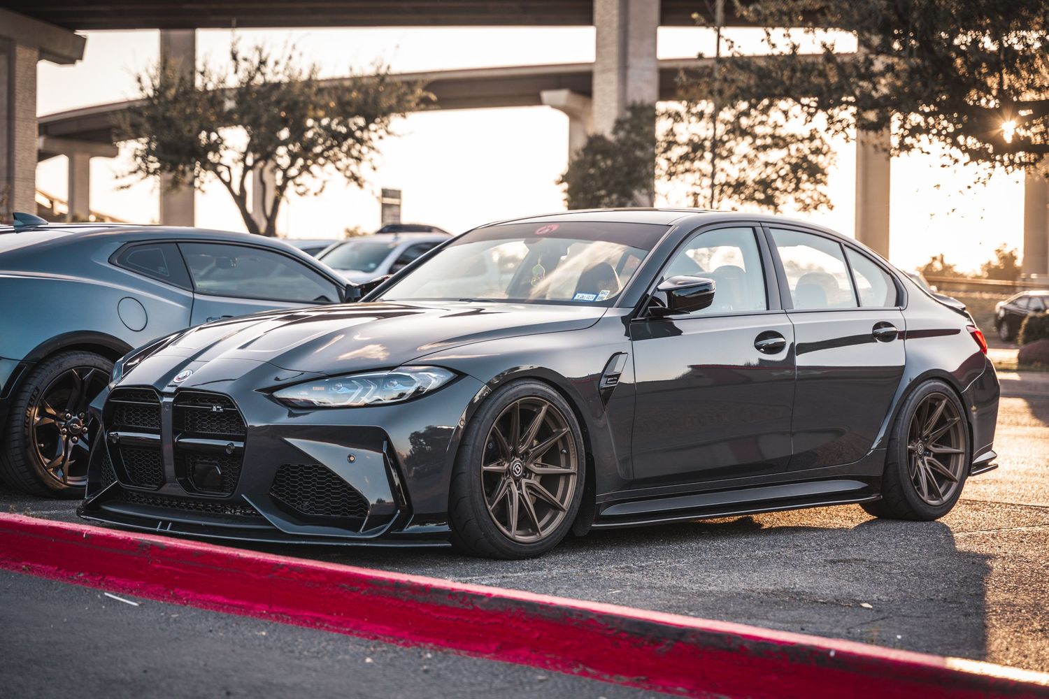 Modified BMW M3 in dark gray with aggressive stance and custom wheels.