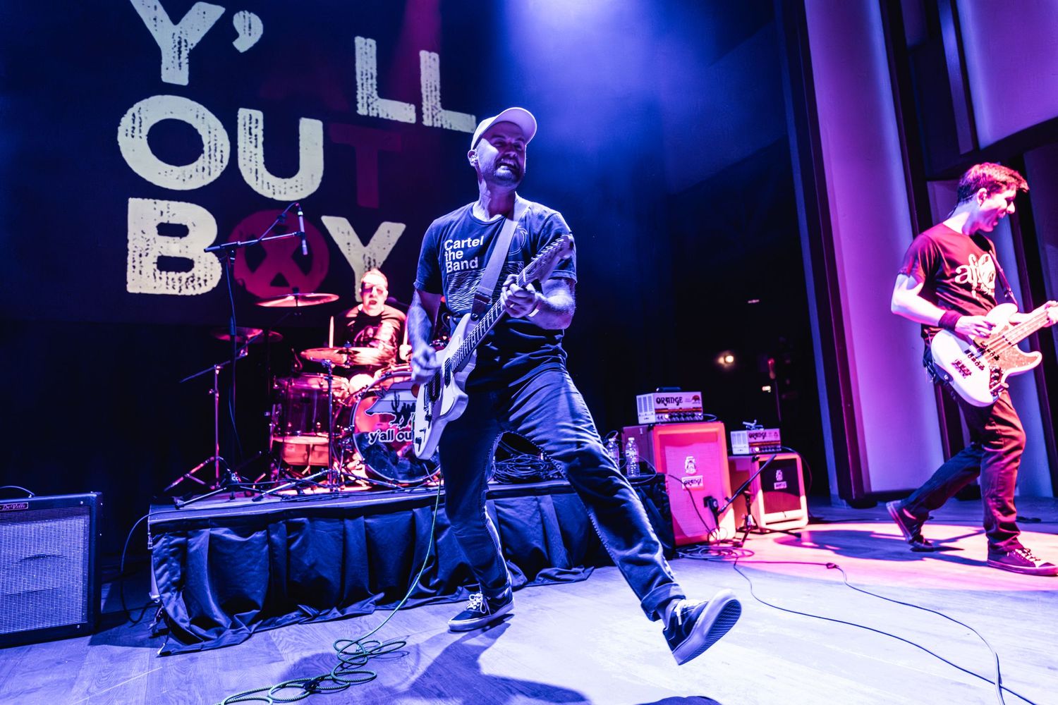Band performs energetically on stage with blue lighting and venue branding visible.