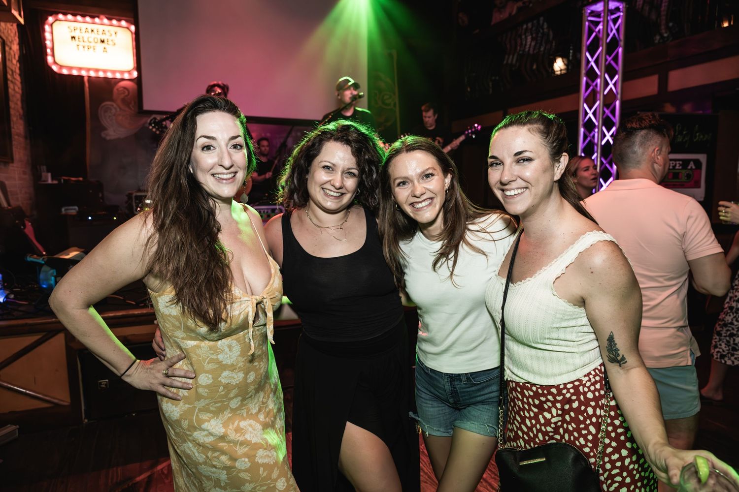 Friends enjoying a night out at a music venue with colorful lighting and stage equipment in the background.
