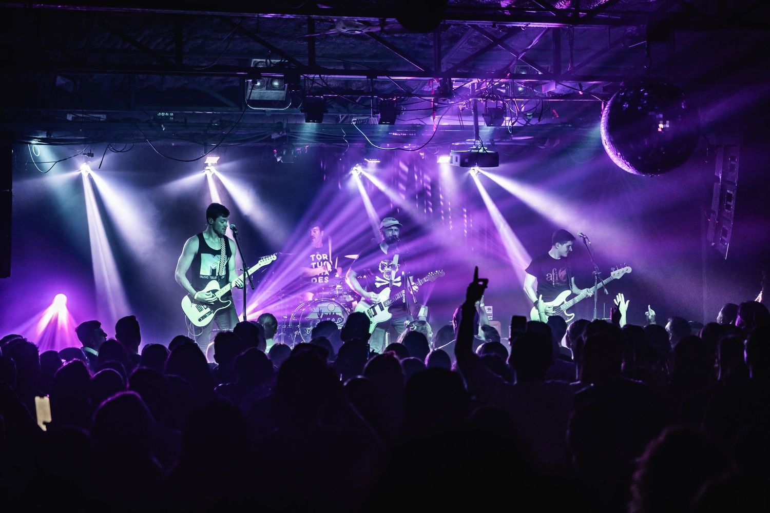 Band plays under dramatic purple and white stage lighting with crowd in silhouette.