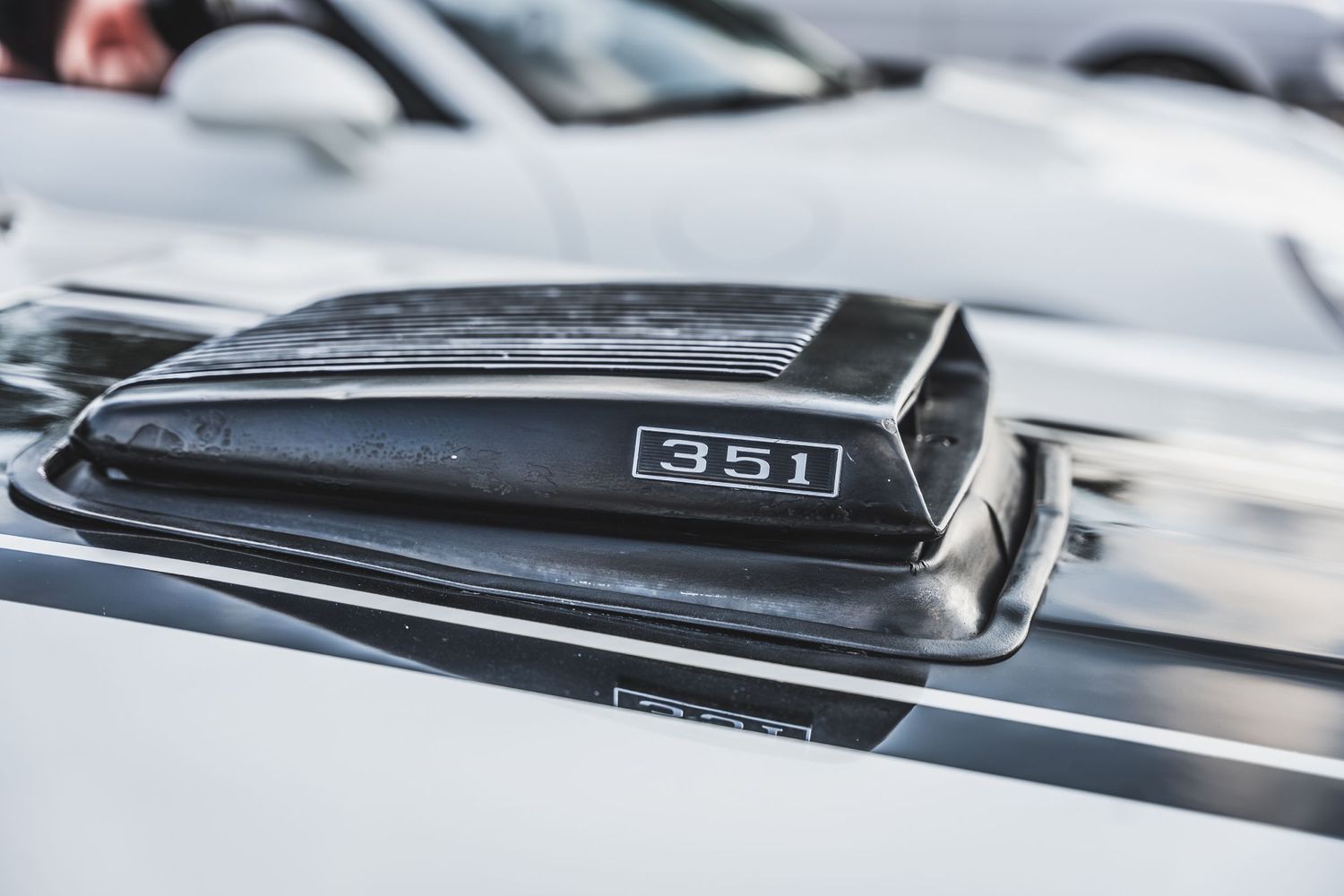 Close-up of Ford 351 hood scoop on white classic car.
