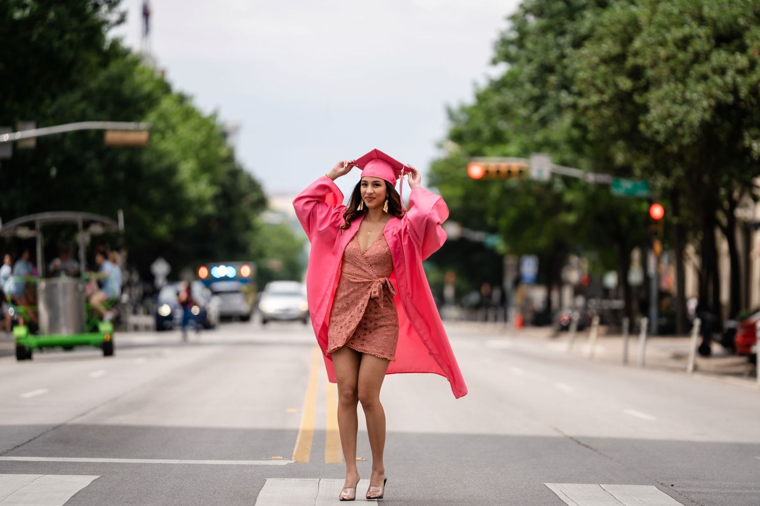 Graduate in pink robe and dress dances joyfully in the middle of a city street.