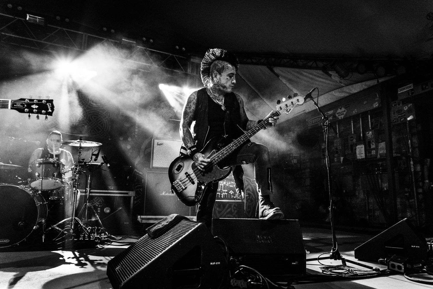 Guitarist performs energetically in black and white photo with dramatic smoke and stage lighting effects.