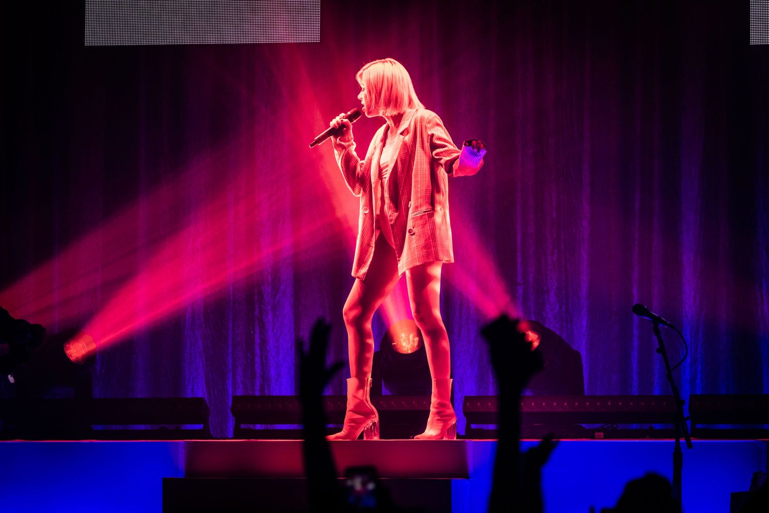 Concert performer in blazer stands on stage bathed in dramatic red and blue lighting.