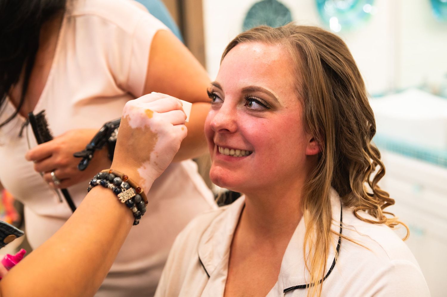Makeup artist applies cosmetics on a smiling subject during wedding preparations.