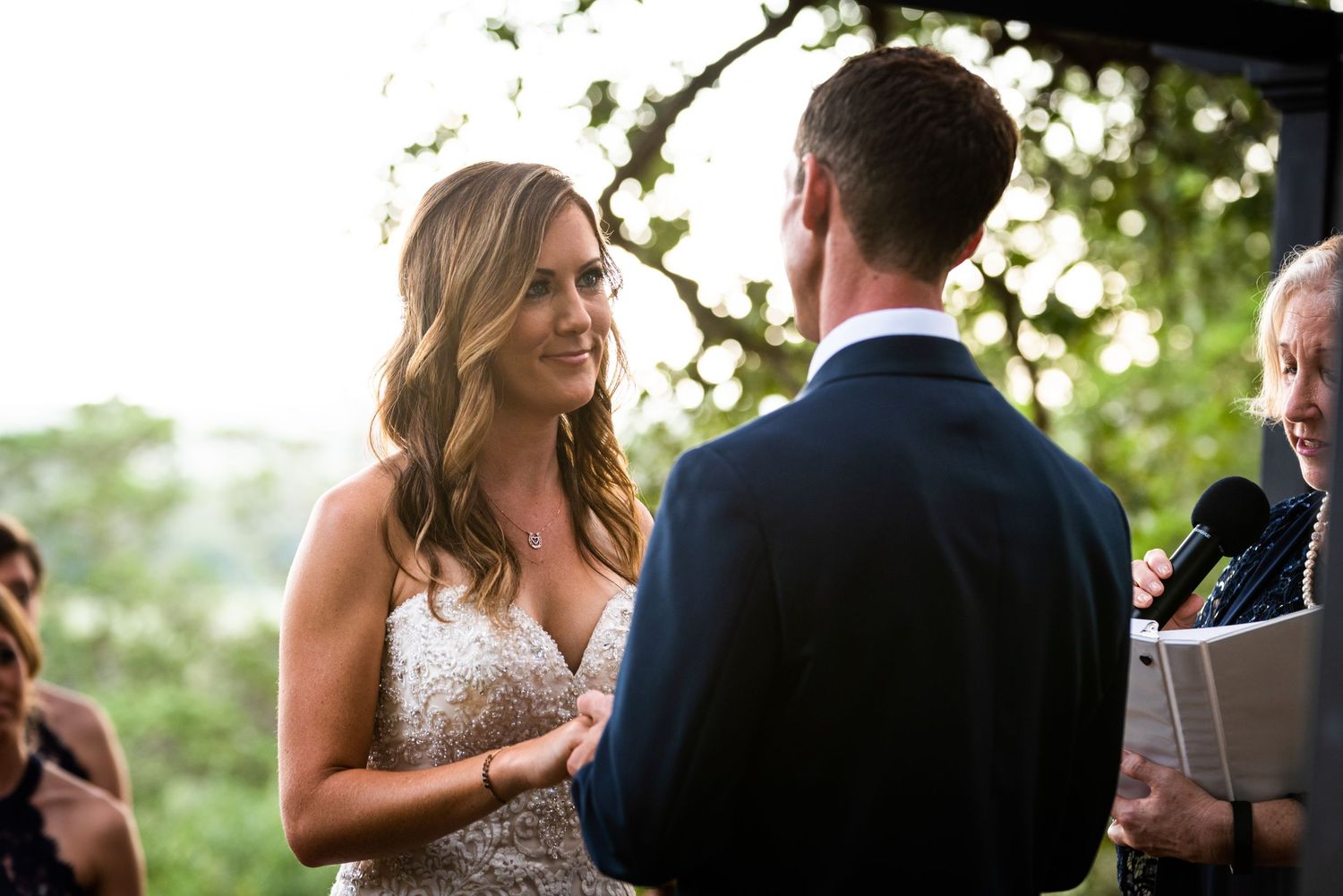 Outdoor wedding ceremony exchange under natural lighting and trees.