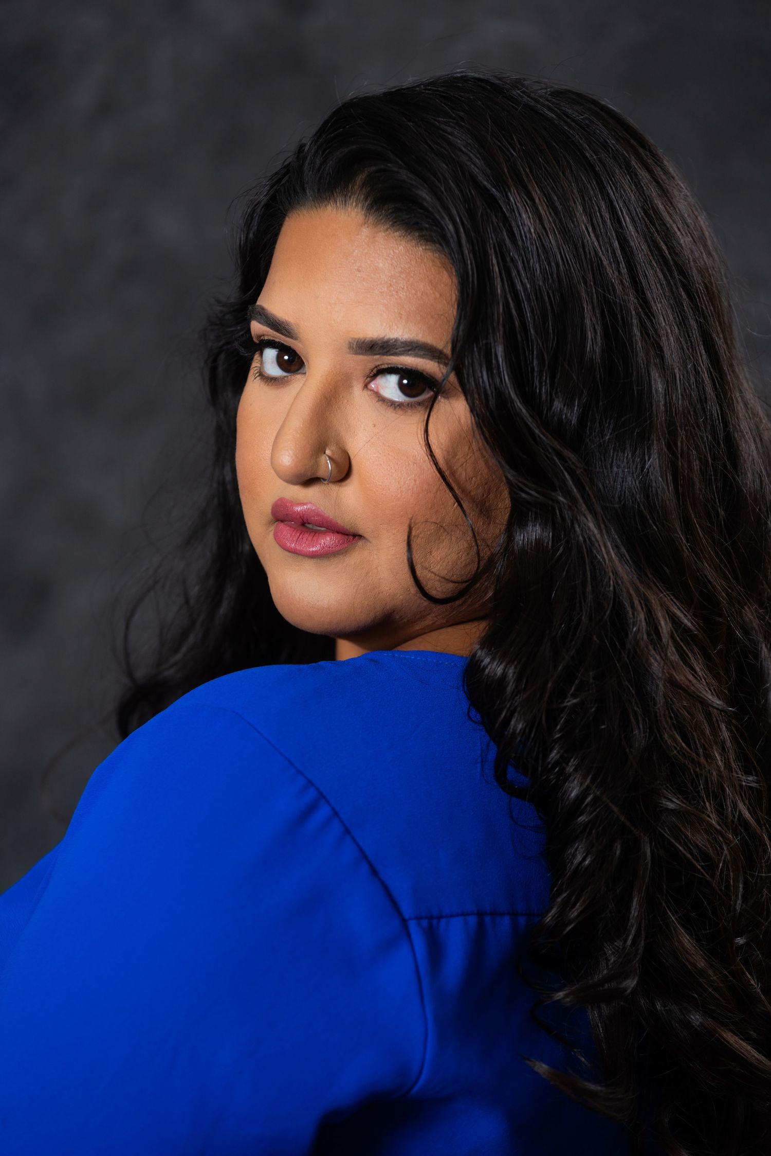 Stylish portrait in vibrant blue with flowing dark hair against dramatic grey background.