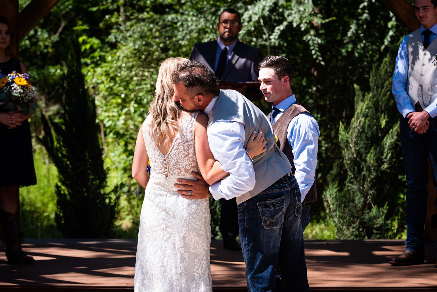 Emotional outdoor wedding ceremony moment under green trees and natural sunlight.