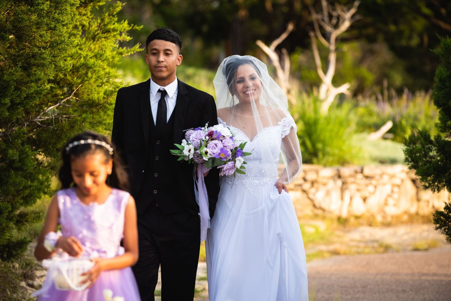 Wedding processional on stone path with flower girl in purple dress.