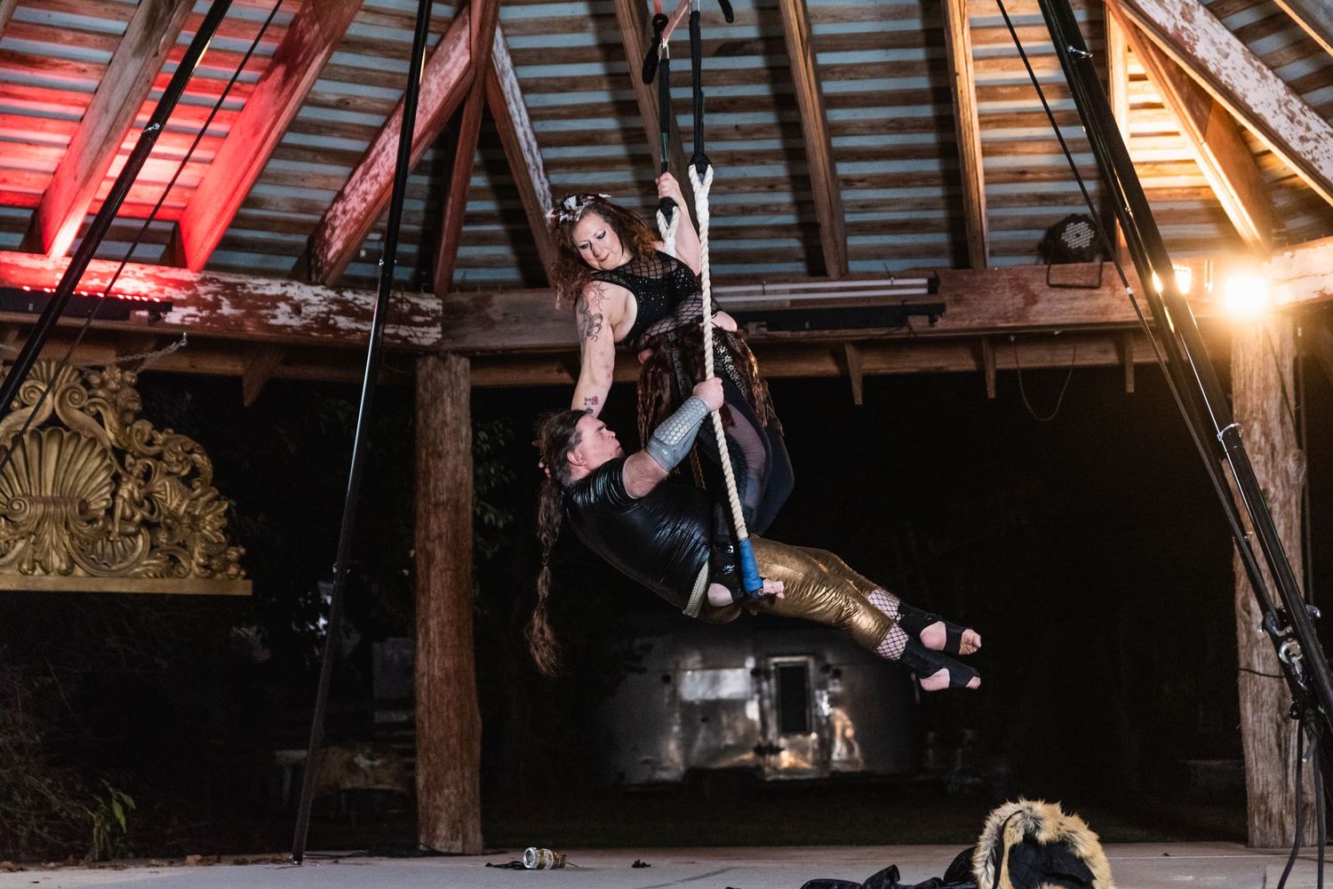 Aerial performer executes dynamic leap in dark rustic venue with dramatic lighting.