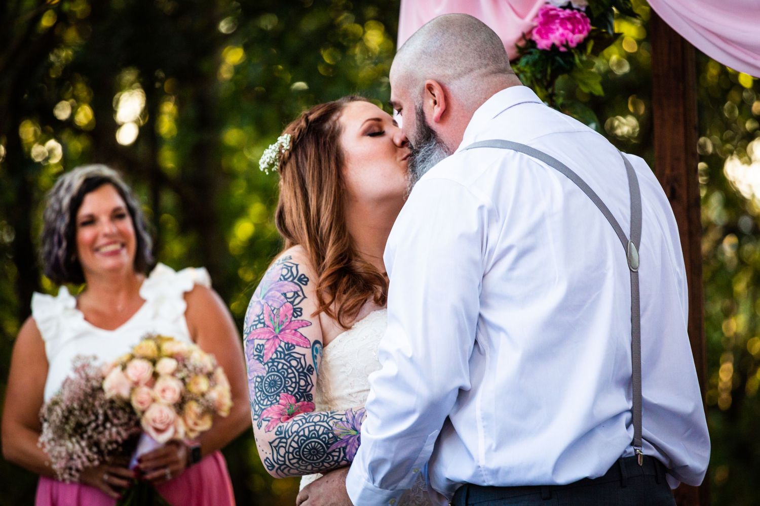 Wedding ceremony moment under pink draped arch with floral decorations.