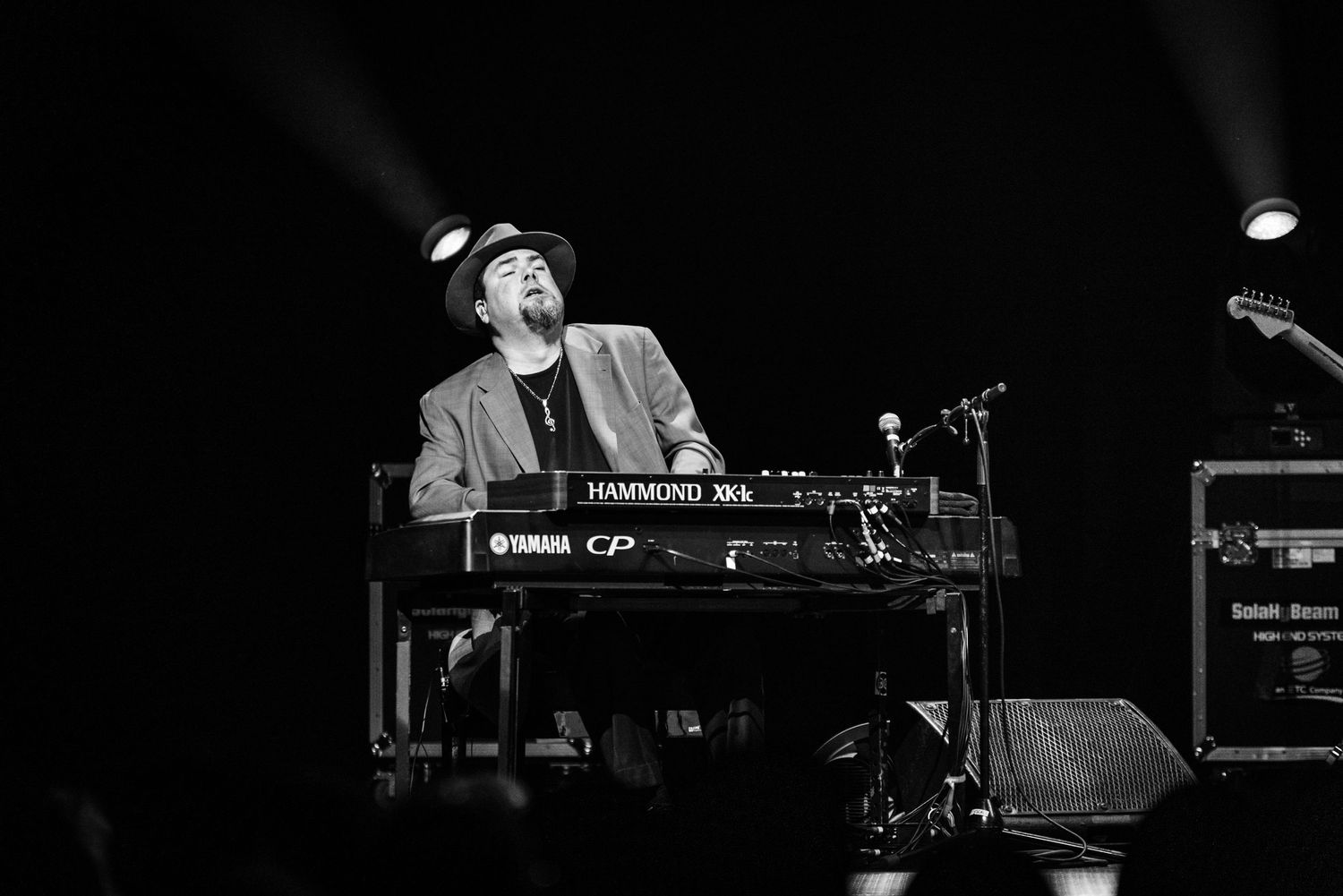 Black and white photo of pianist performing at keyboard on darkened stage.
