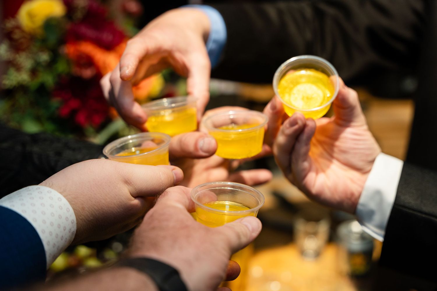 Multiple hands toasting with orange cocktails in elegant glasses.