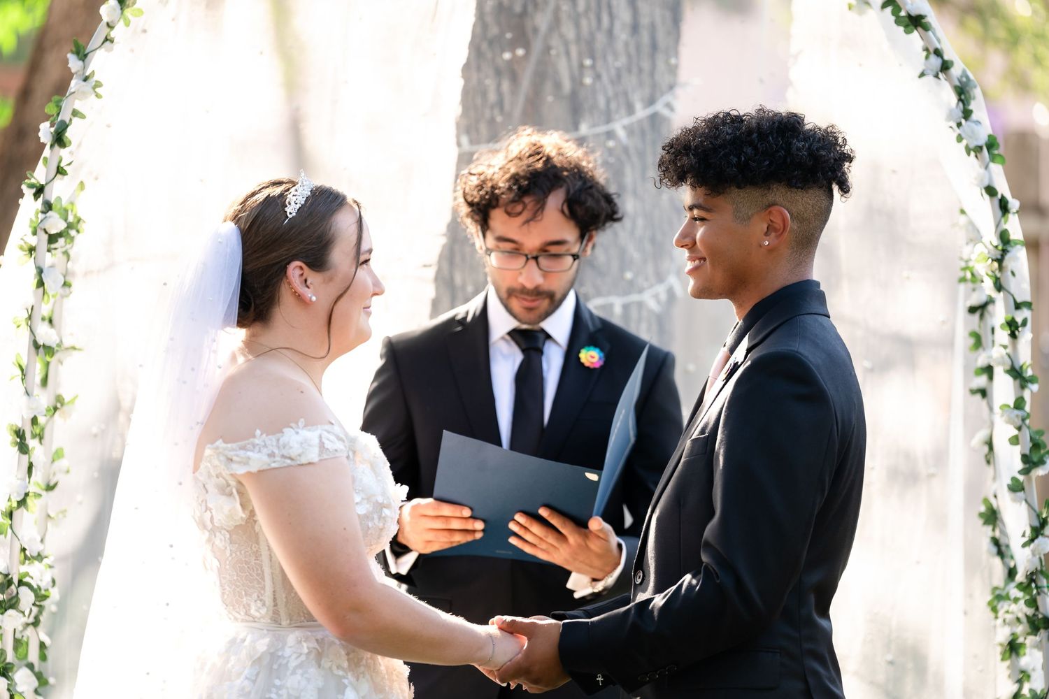 Wedding ceremony under a decorated arch with the officiant holding a folder during the service.