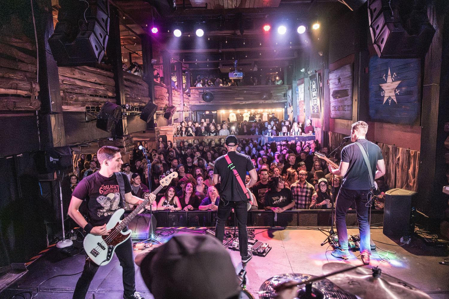 Wide shot of band performing on stage with large crowd at music venue.