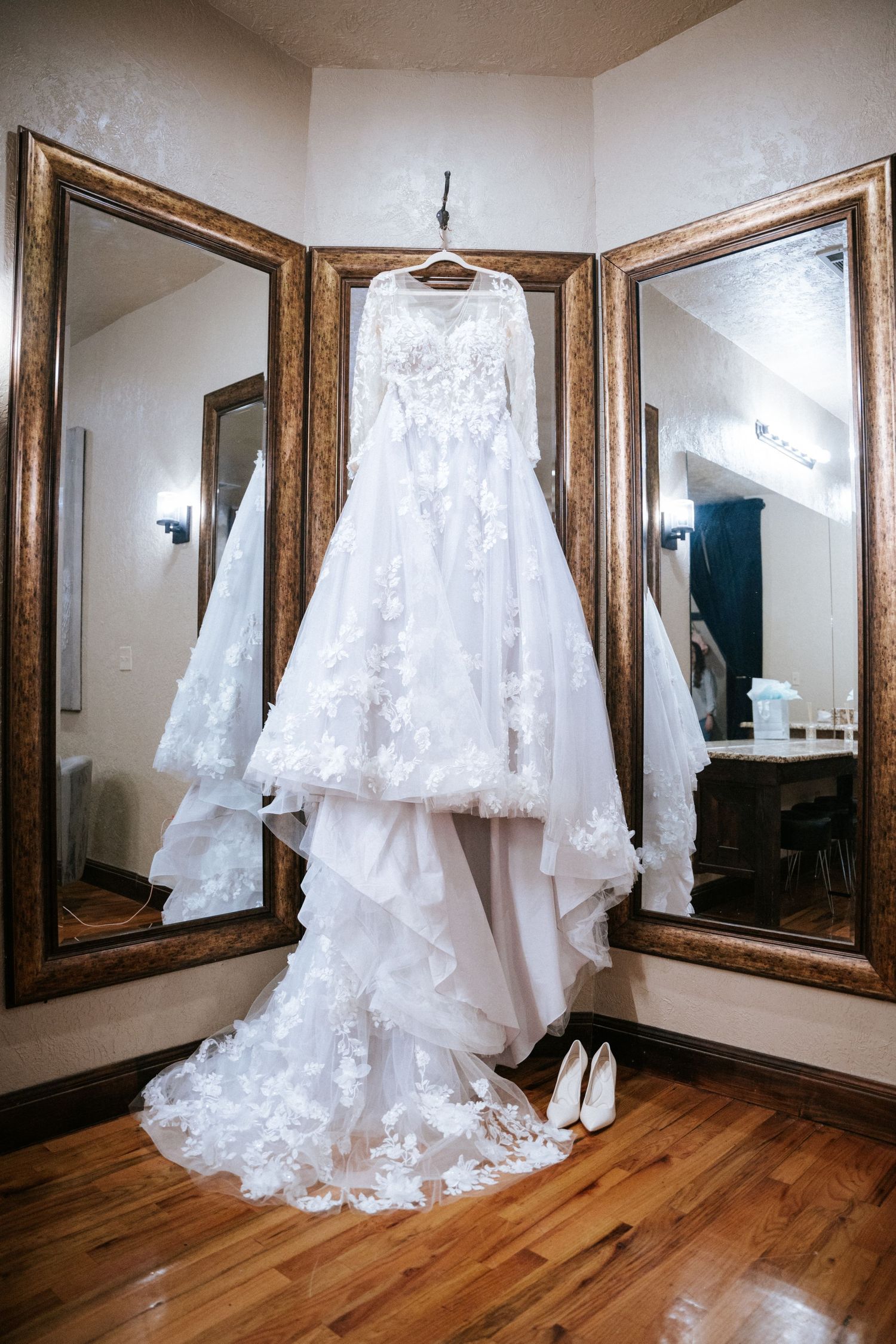 White lace wedding dress displayed on hanger between ornate full-length mirrors.