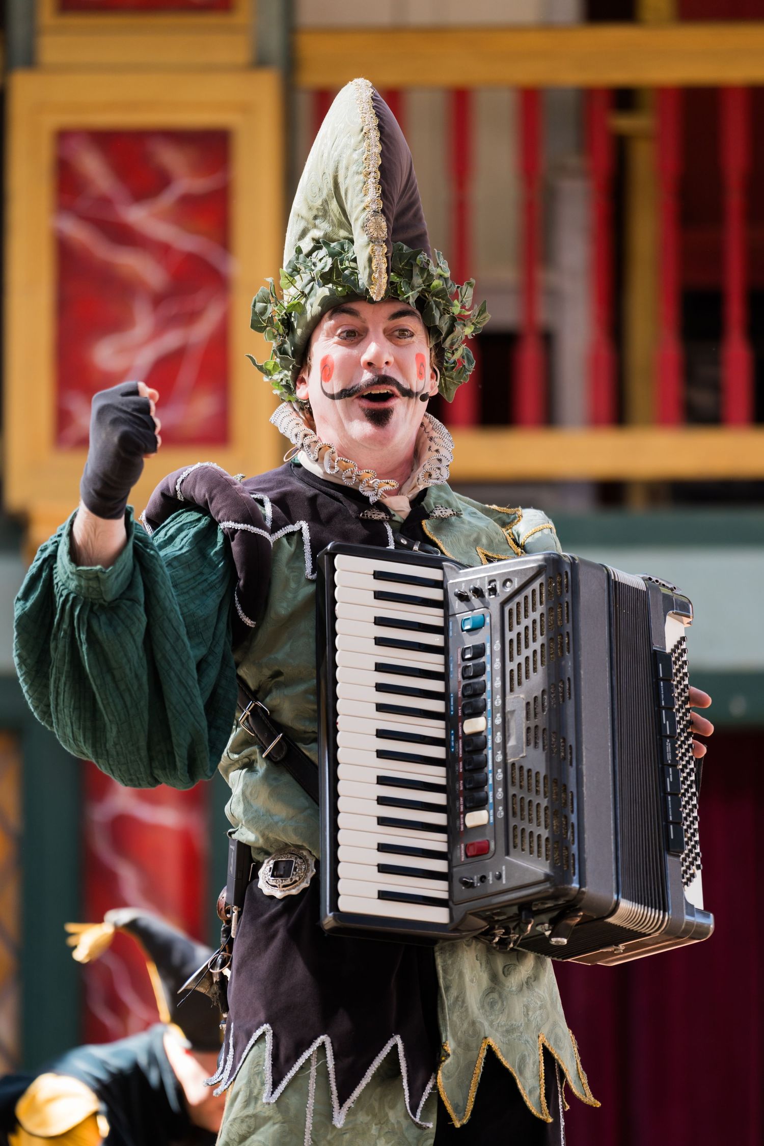 A costumed performer in a pointed hat plays accordion while entertaining at a Renaissance festival.