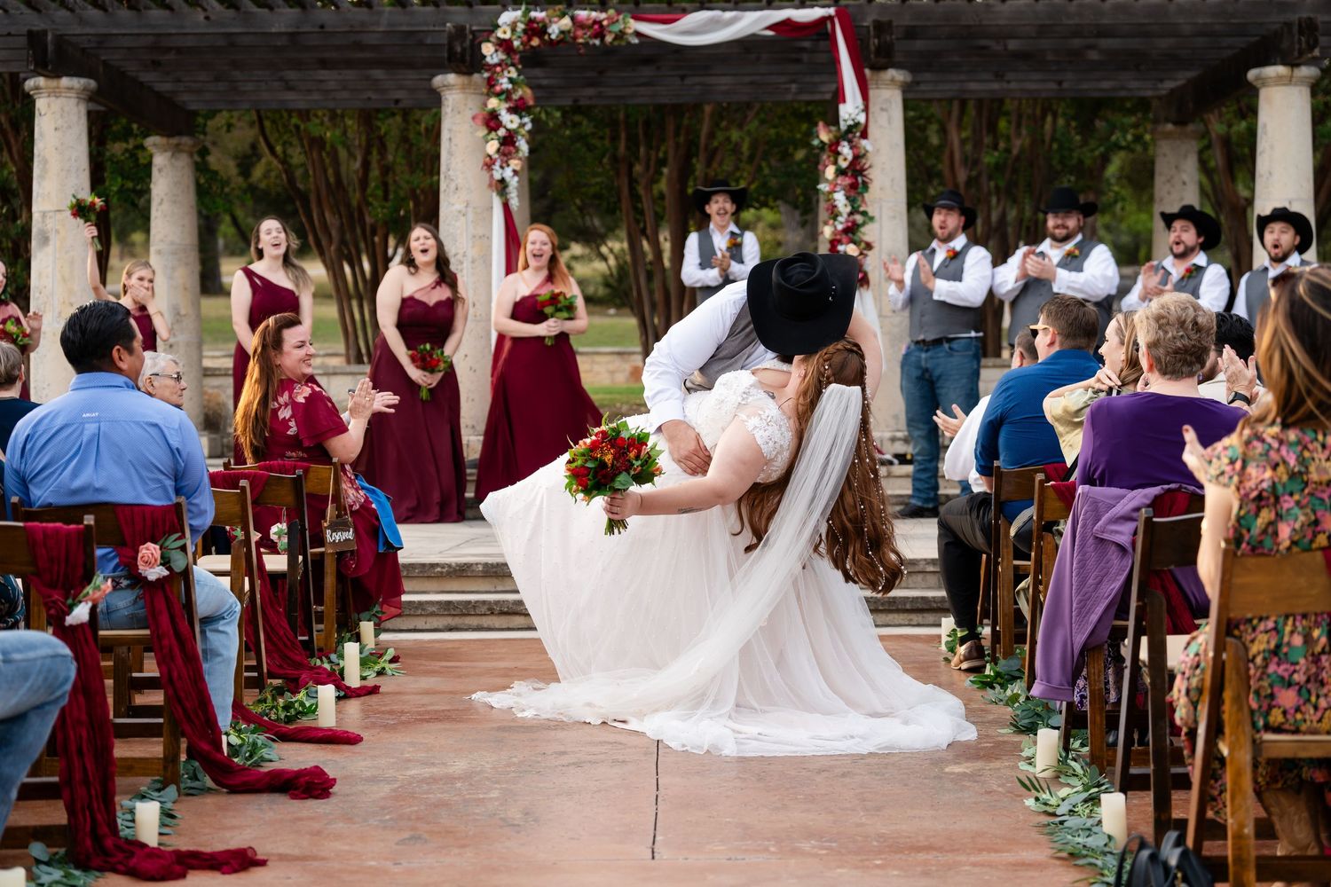A dramatic dip kiss during an outdoor wedding ceremony with guests seated on both sides.