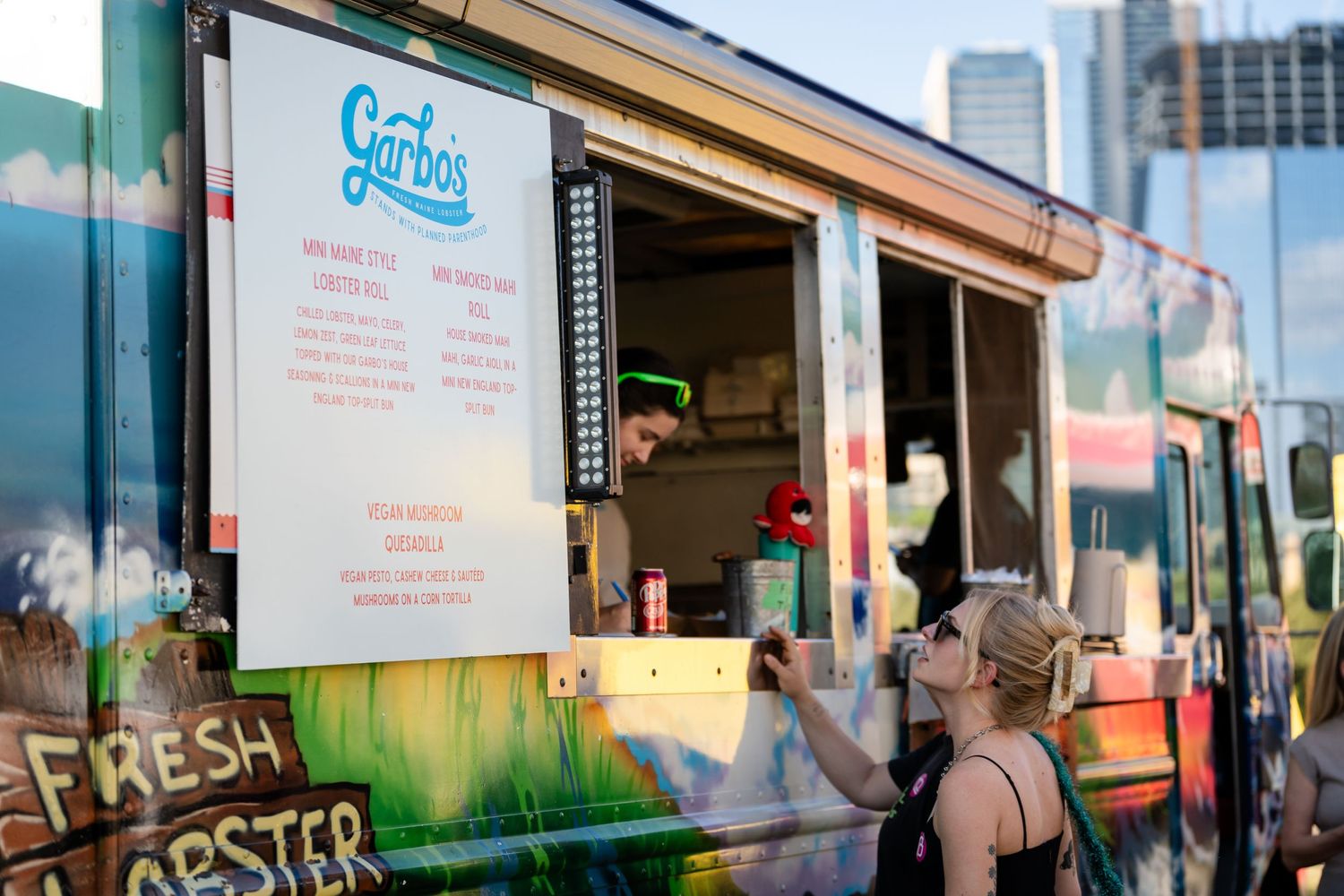 Food truck with menu board serving customers at an outdoor event.